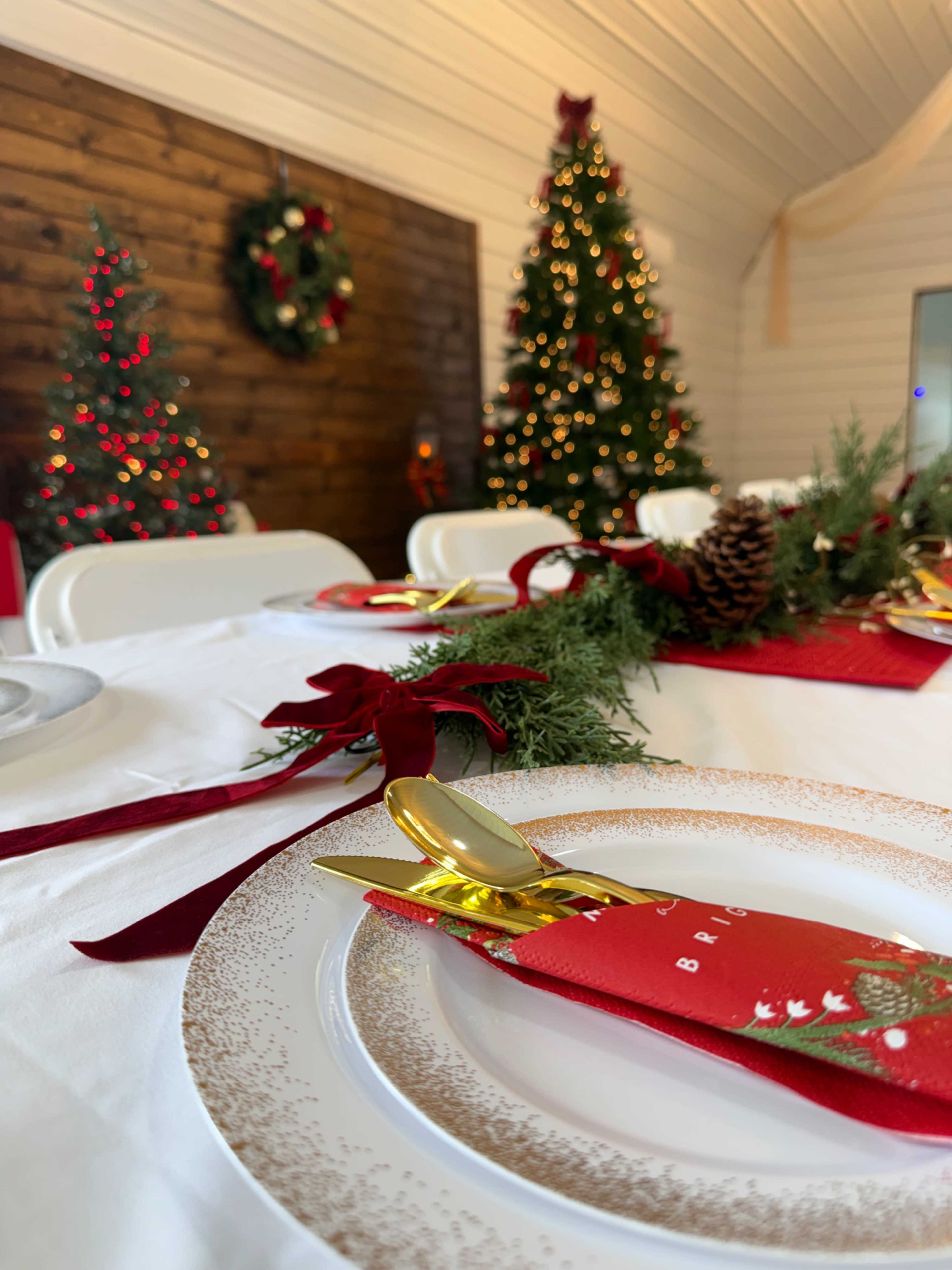 The image shows a festive dining setup with decorated tables, red napkins, golden cutlery, and Christmas trees adorned with lights in the background.