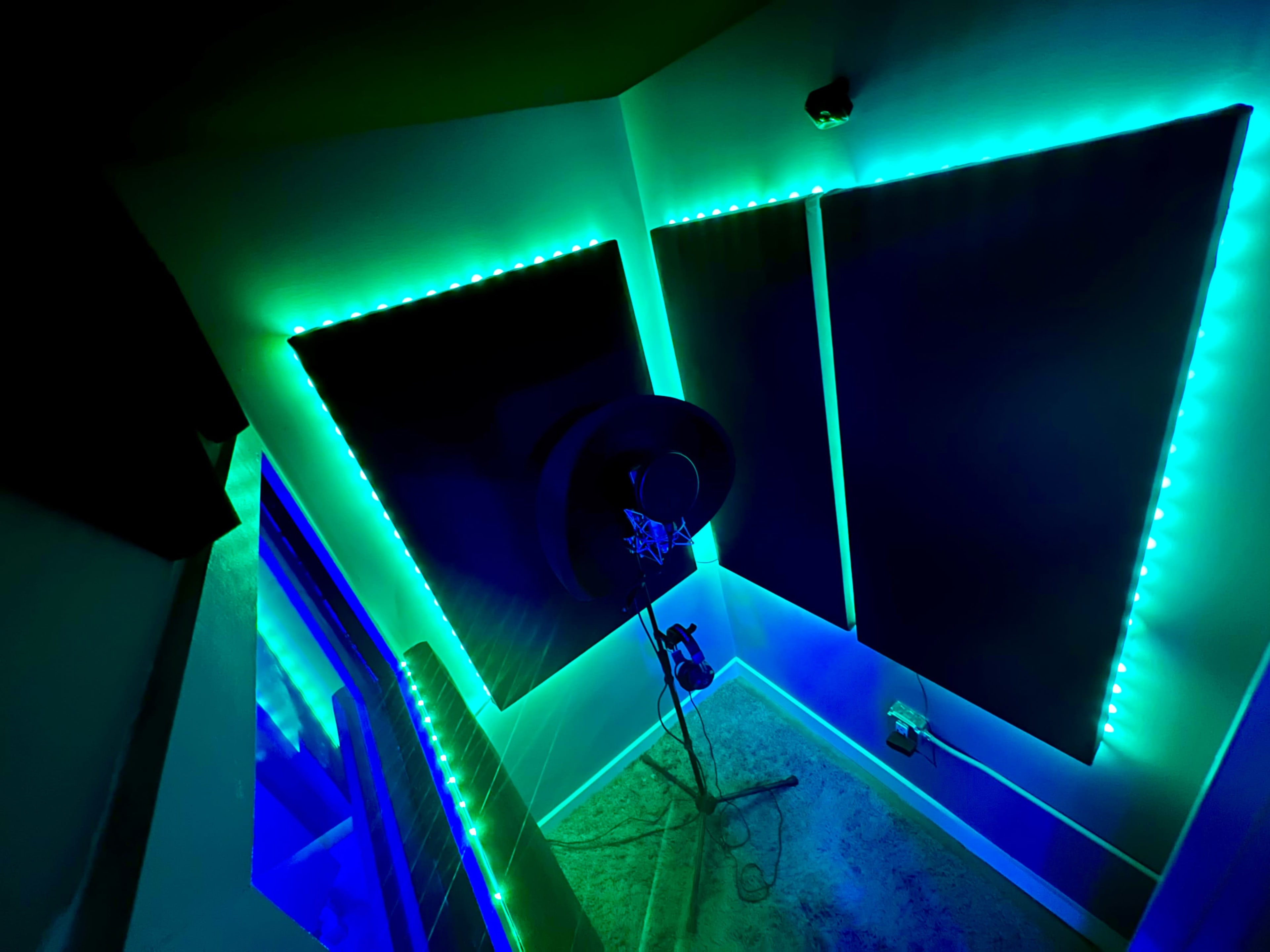 The image shows a small recording booth with soundproof panels and neon blue-green LED lights.