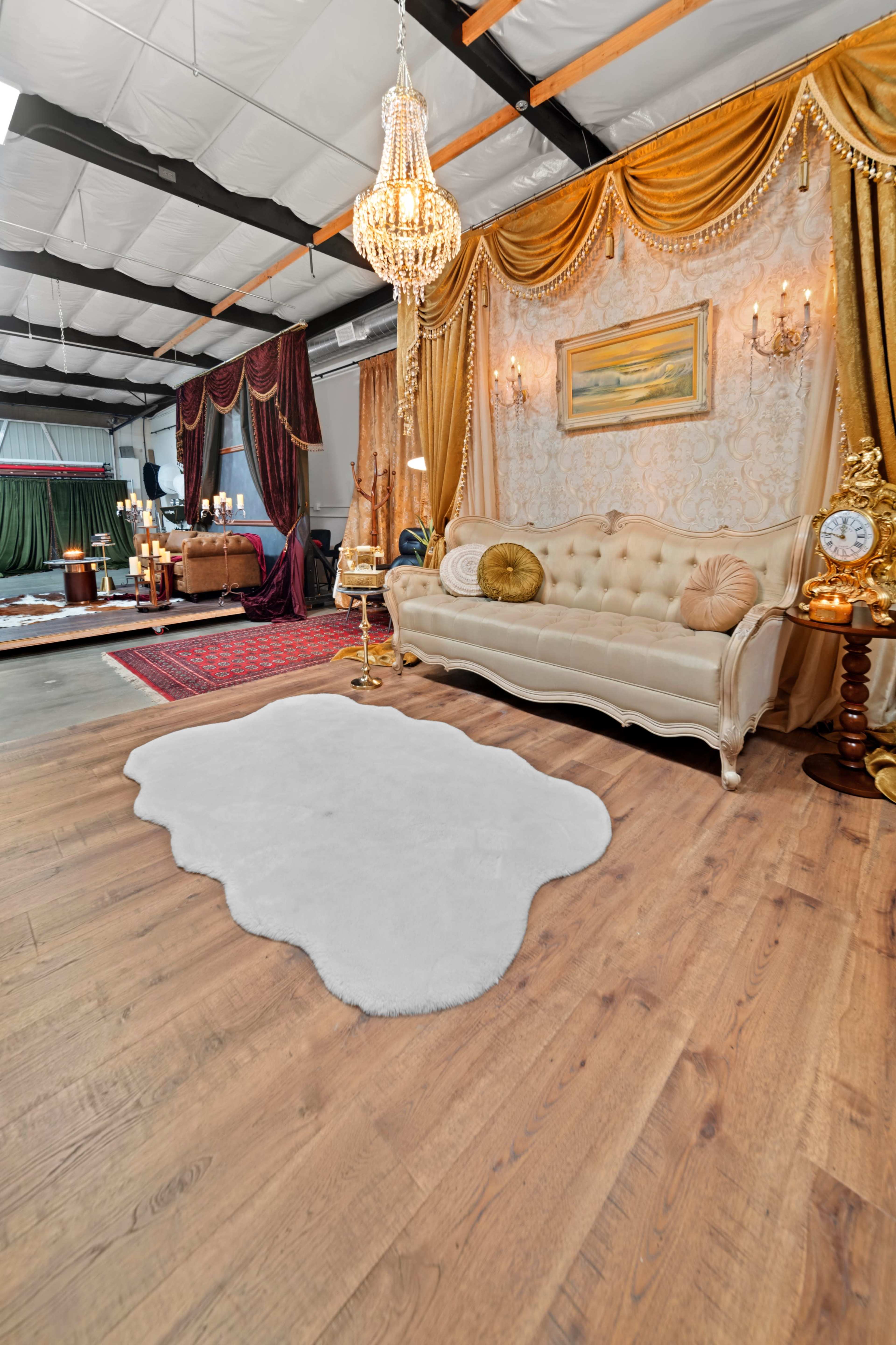 The scene features an elegantly decorated room with a plush white rug, a vintage-style sofa, ornate drapes, and decorative lighting fixtures.