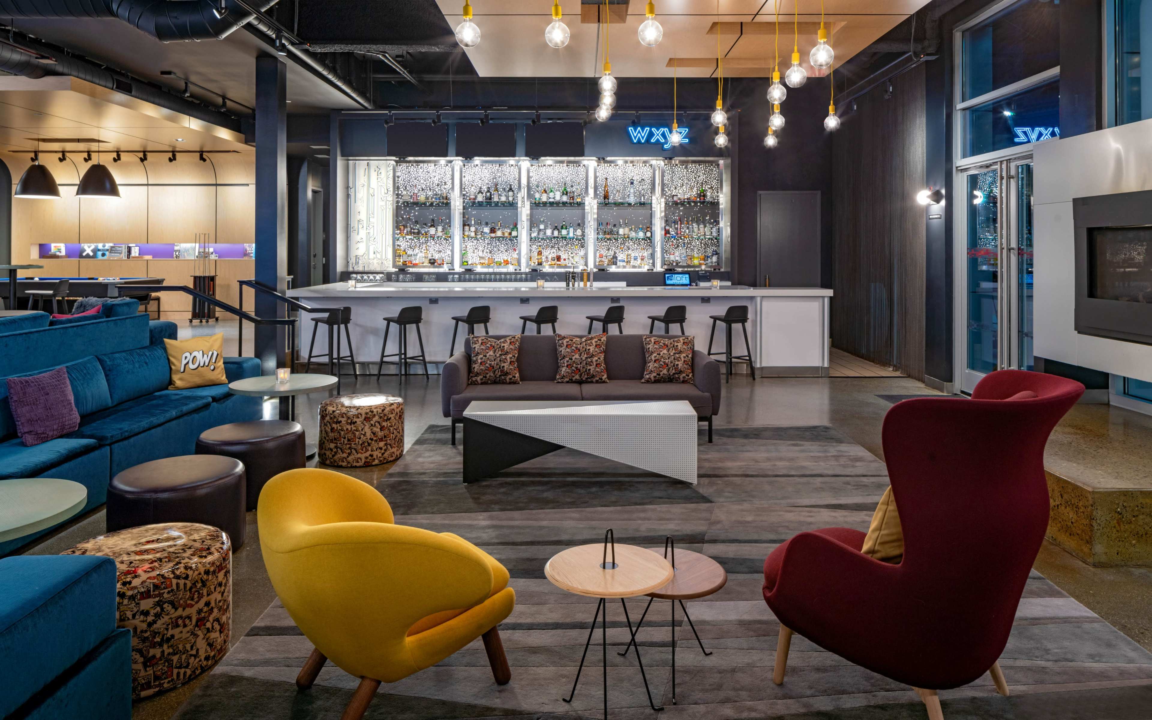 A modern lounge area with a bar featuring backlit shelves of liquor, colorful seating arrangements, and a contemporary design.