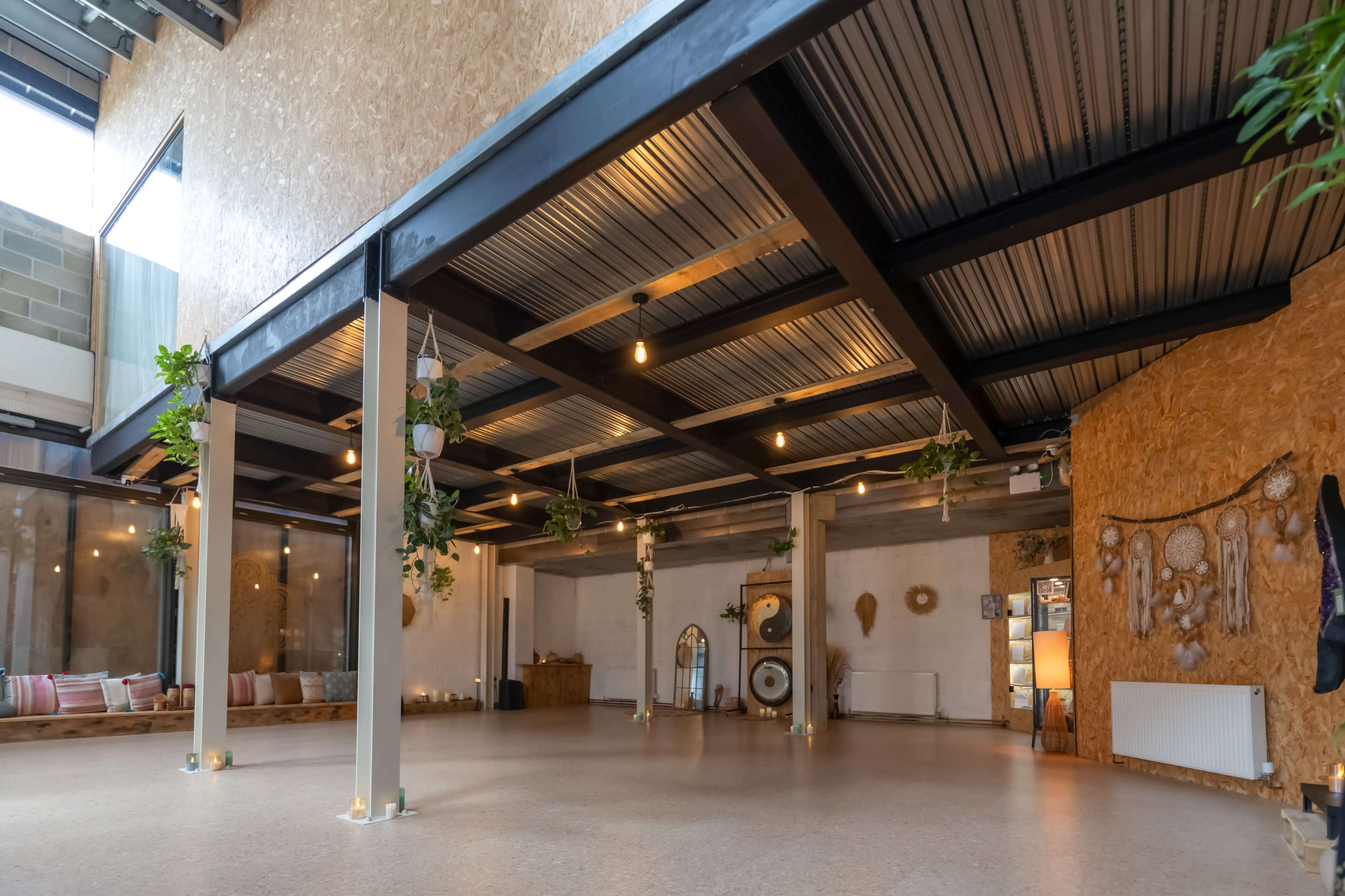 The image shows a spacious interior with a polished floor, exposed metal beams, and decorative plants hanging from the ceiling.