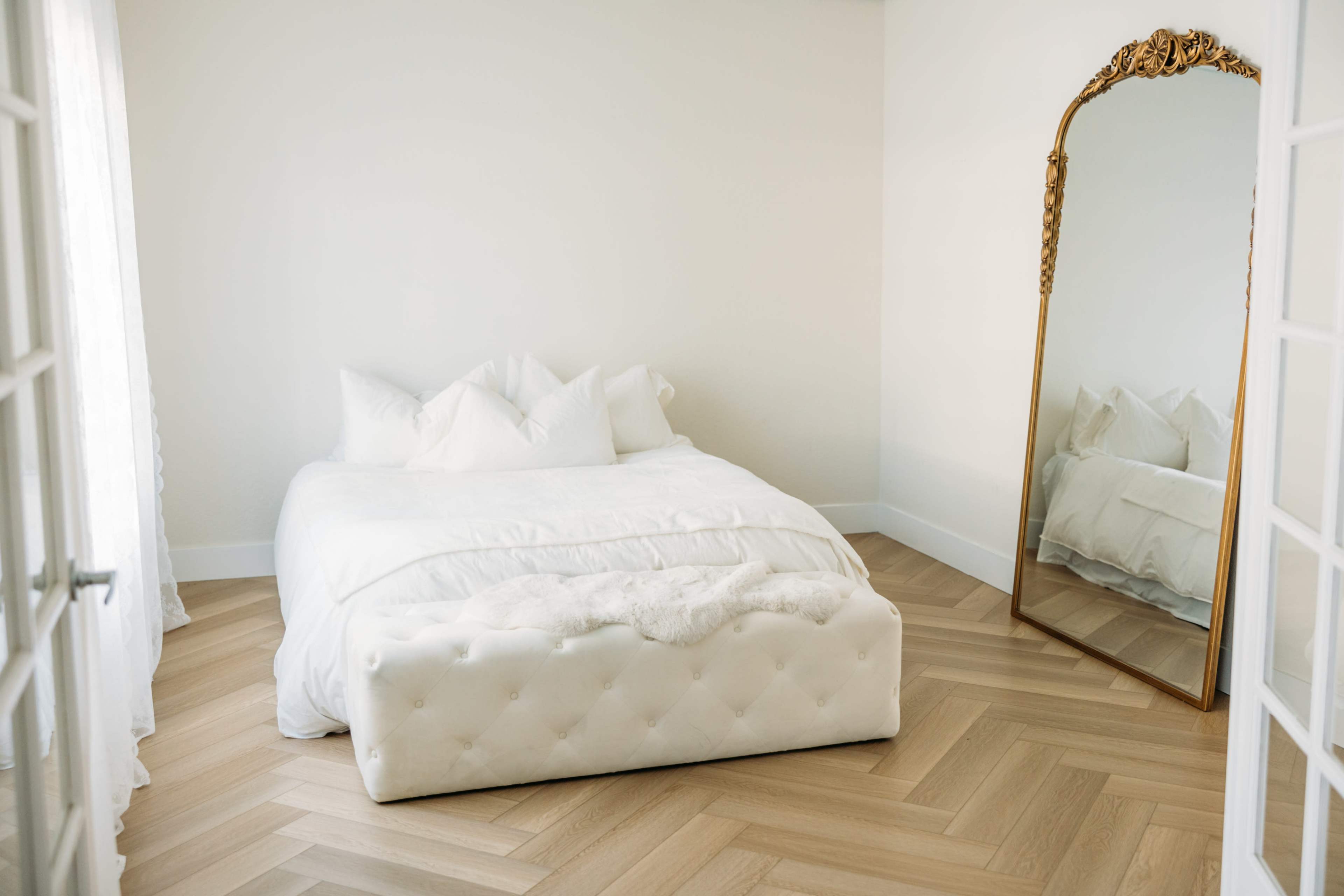 A neatly arranged bedroom features a white bed with decorative pillows and a large mirror against a light-colored wall.
