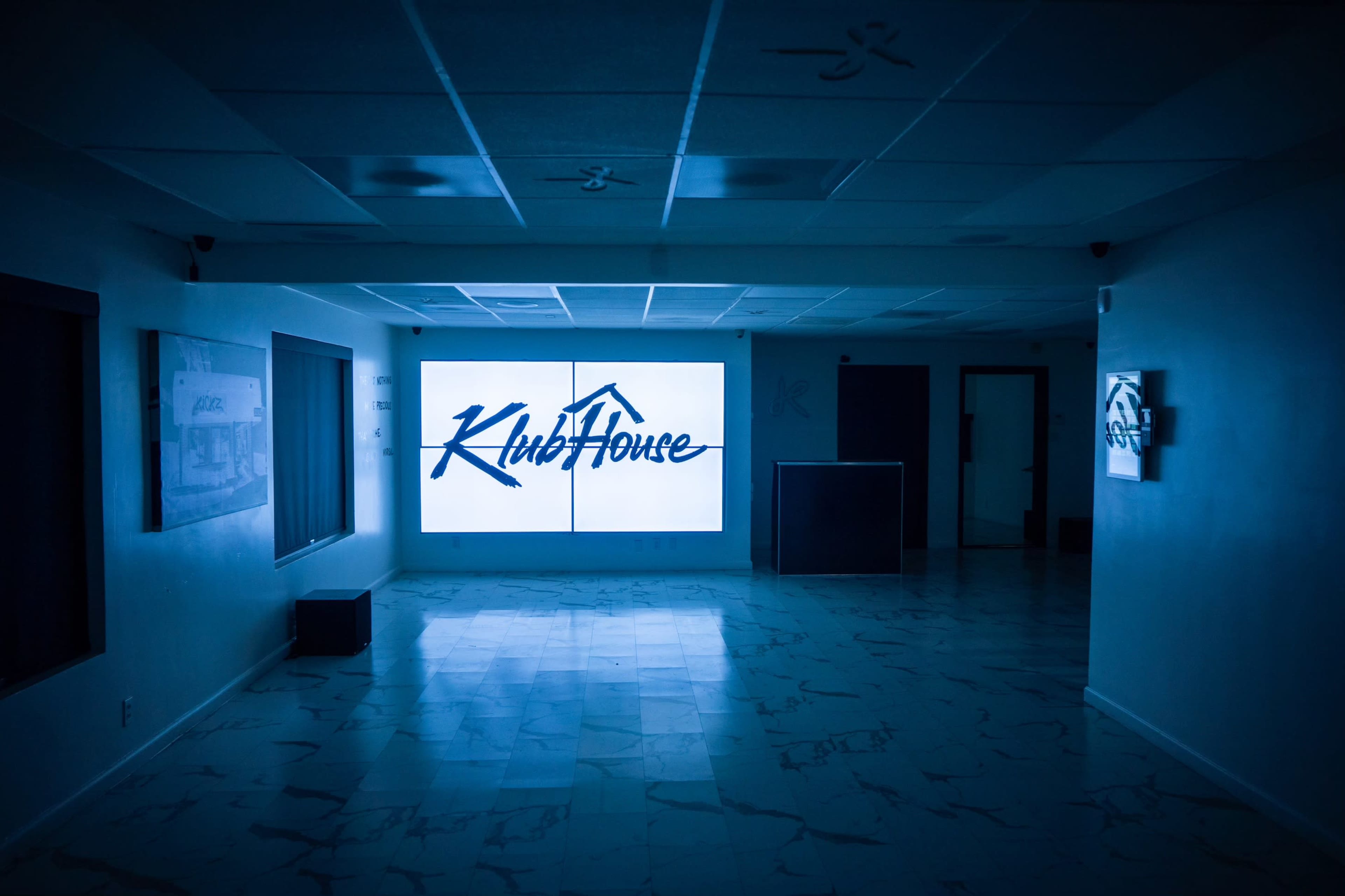 The image shows an empty, dimly lit interior space with a large illuminated sign reading "KlubHouse" on a wall.