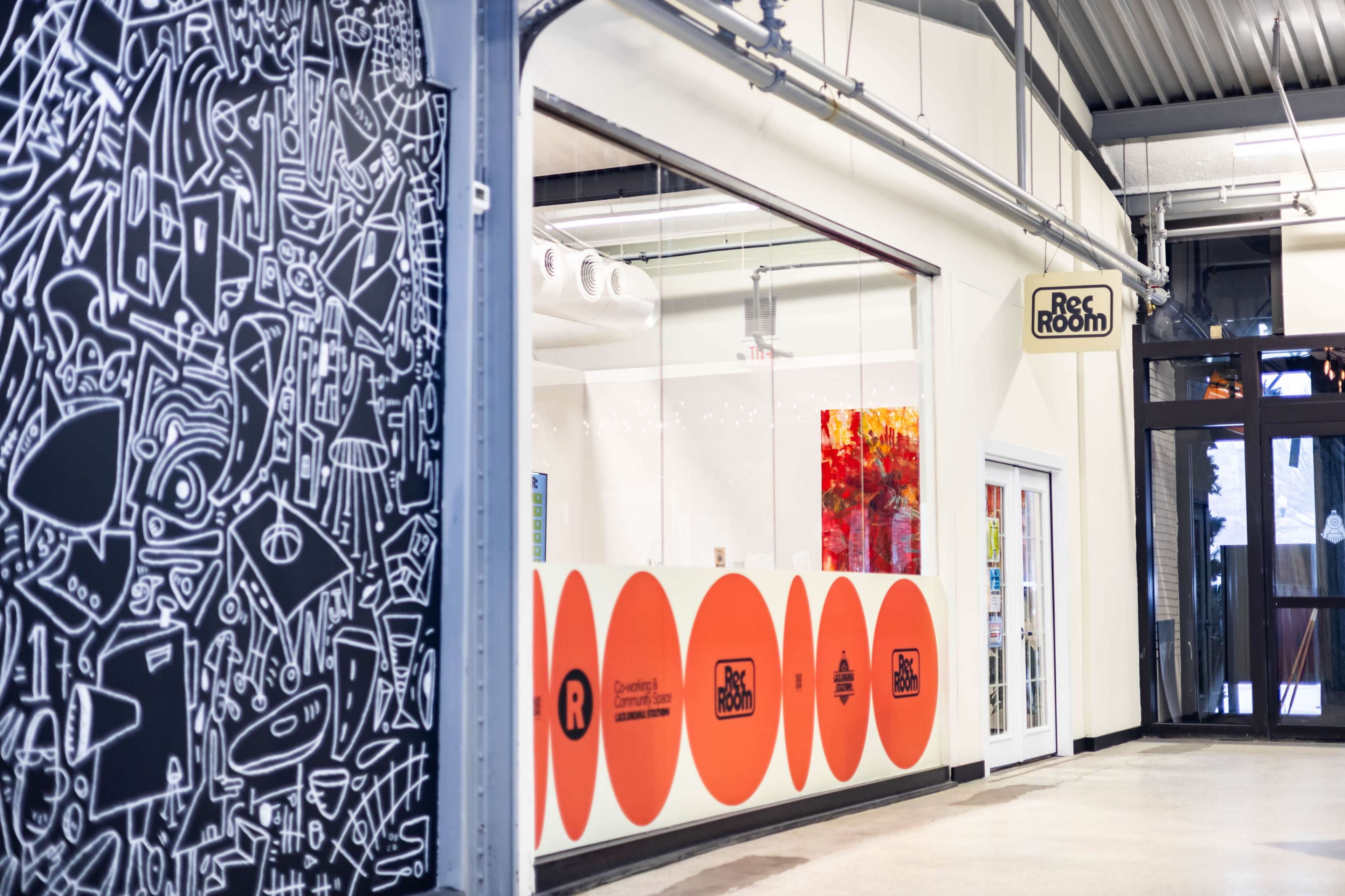 The image shows a modern indoor space with a bold black-and-white mural on one side and a series of large orange circles featuring the text "Rec Room" on the wall opposite.