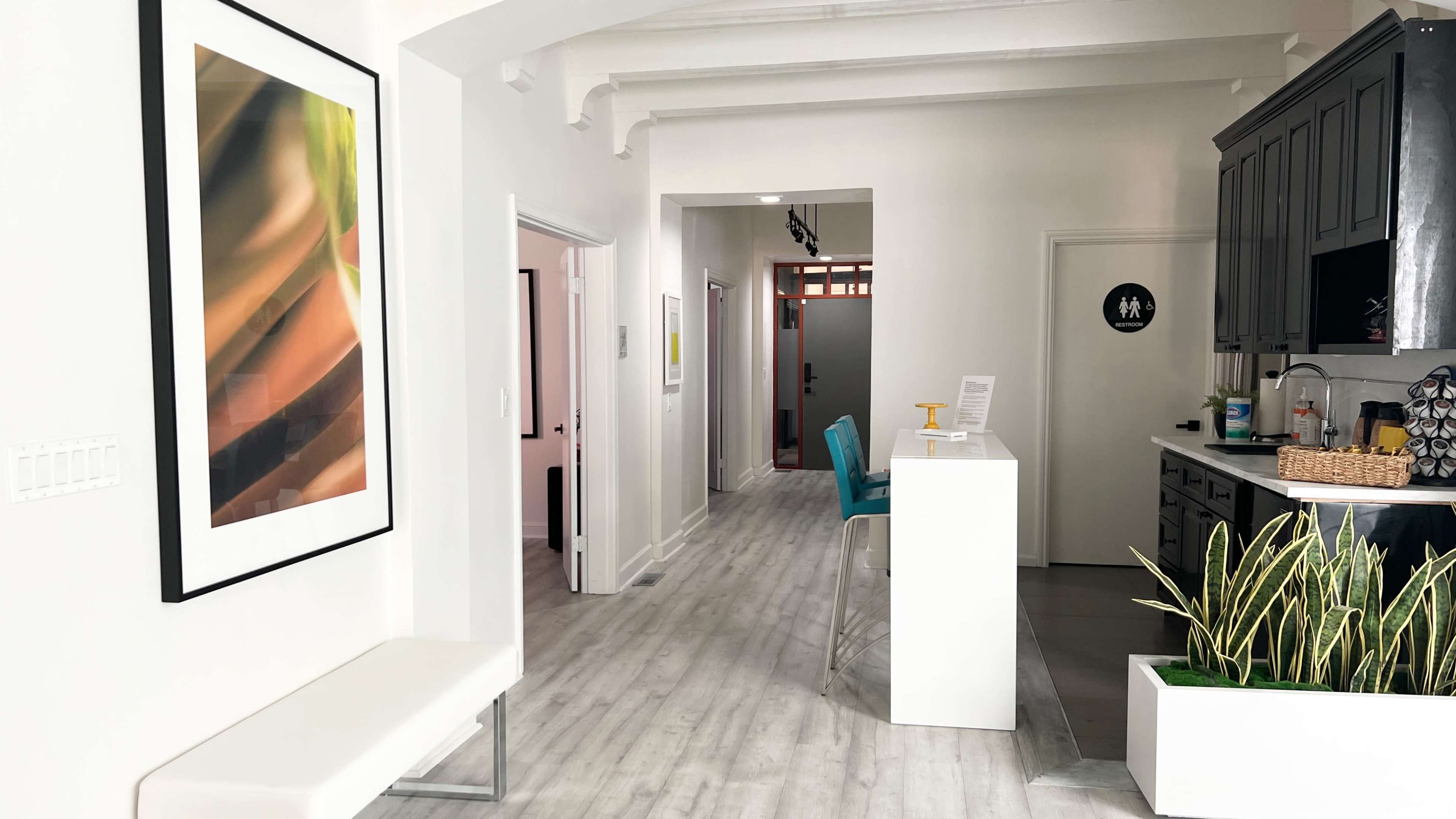 A modern, airy interior space with a white bench, a reception area with a service counter, and a corridor leading to additional rooms.
