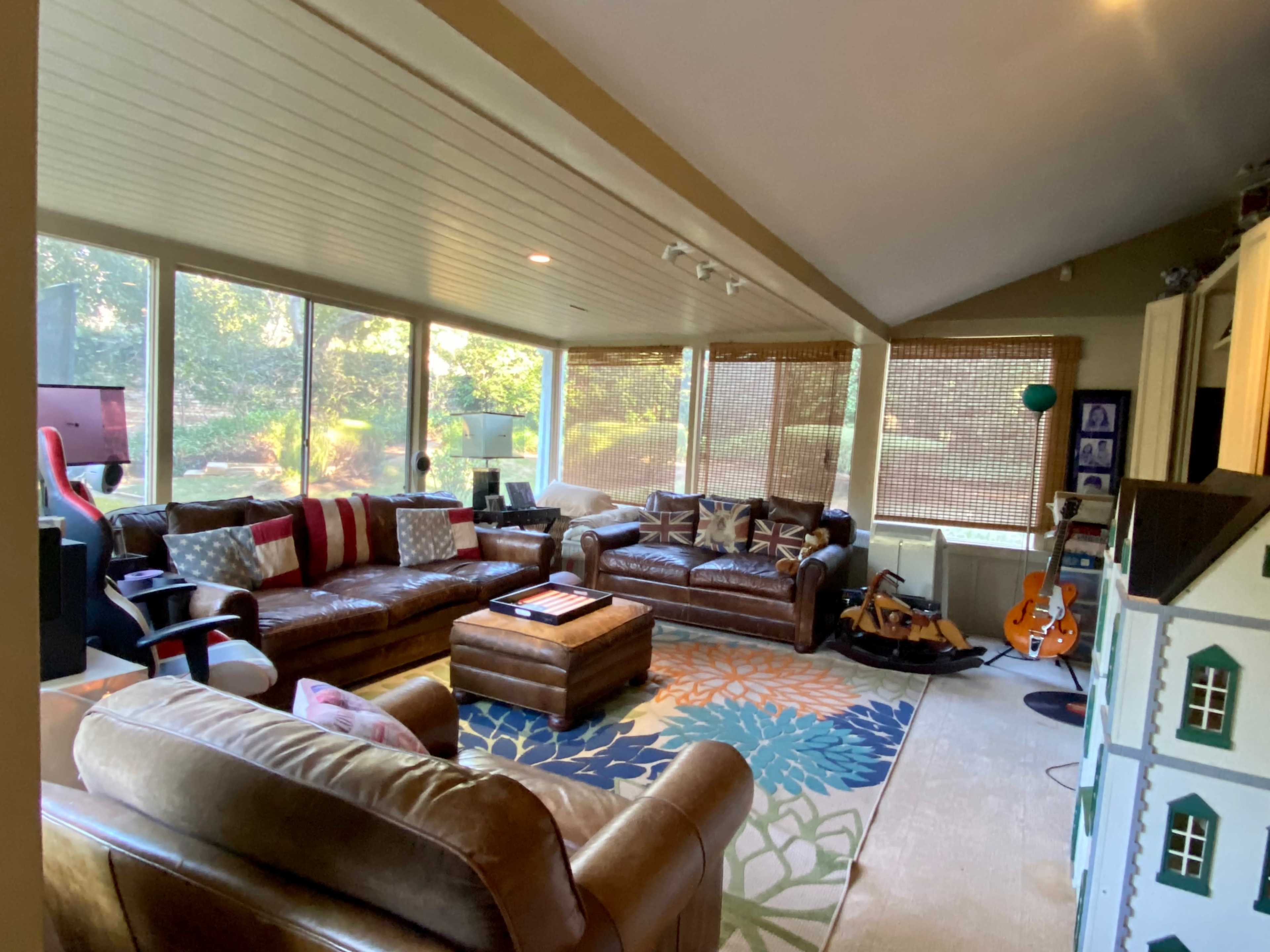 A spacious living room with large windows, a variety of seating options including brown leather sofas, and a colorful area rug.
