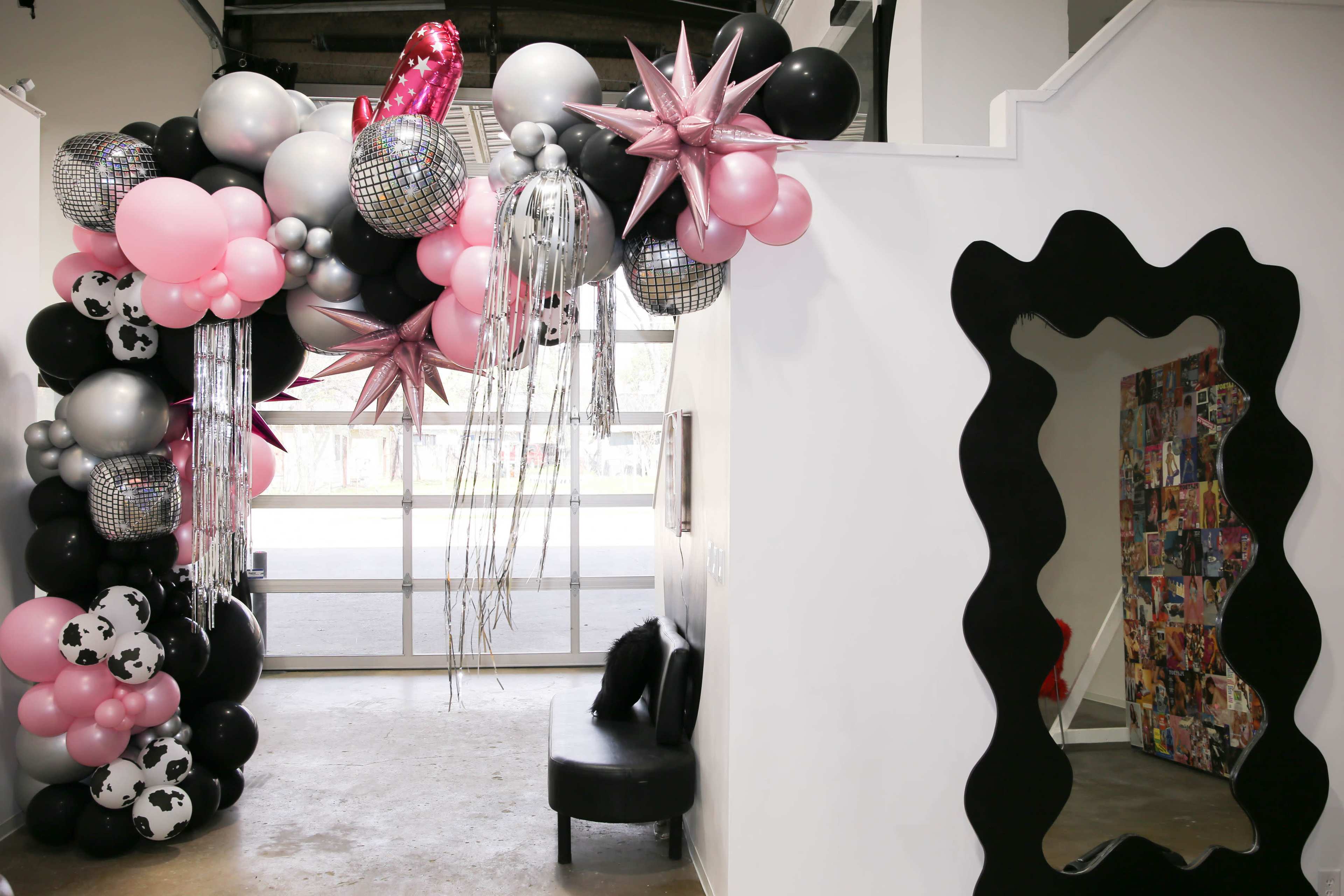 A colorful balloon arch with metallic accents and a large mirror is positioned at the entrance of a room.