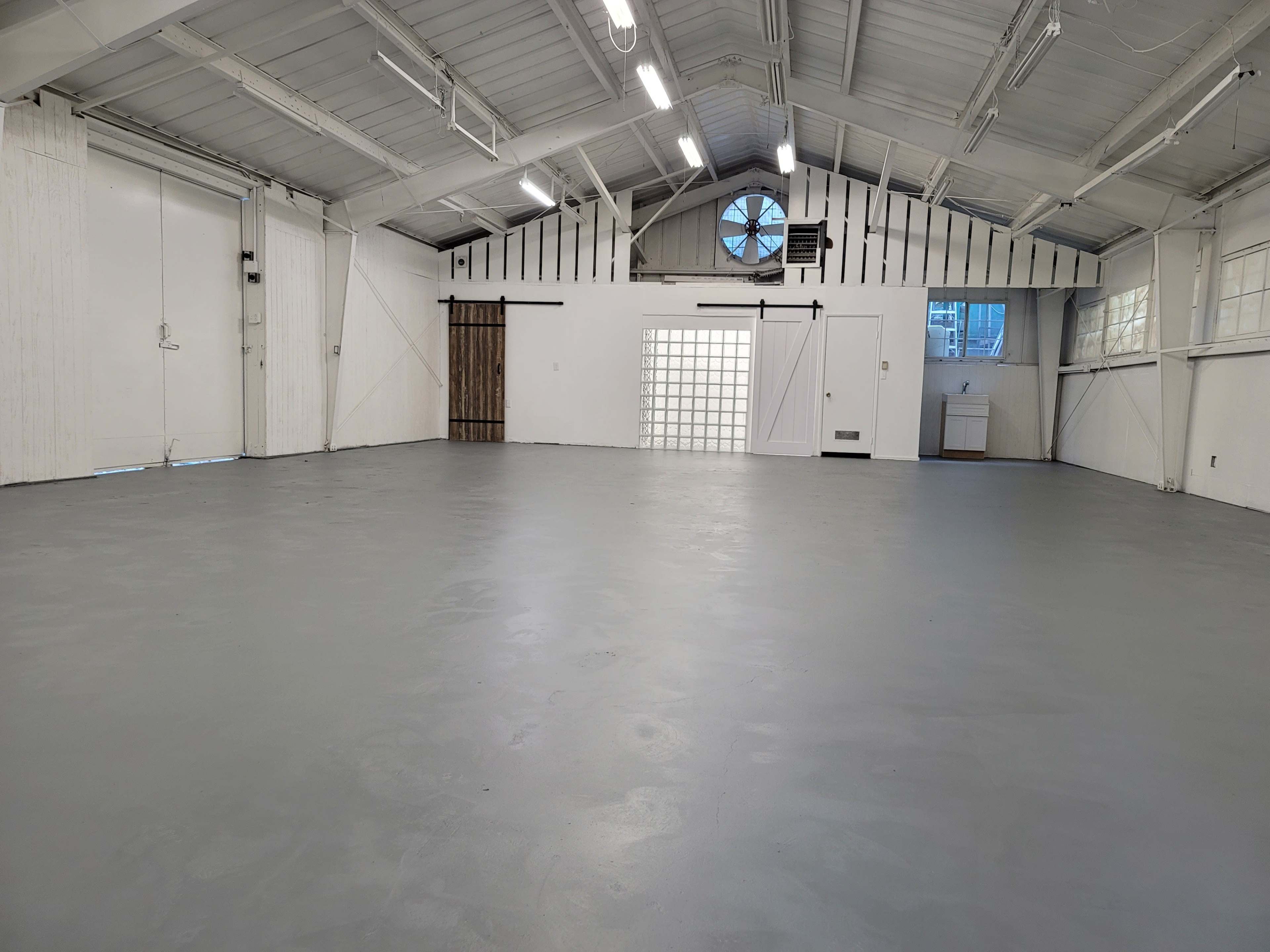 An empty industrial space with gray flooring and large windows allowing natural light to enter.