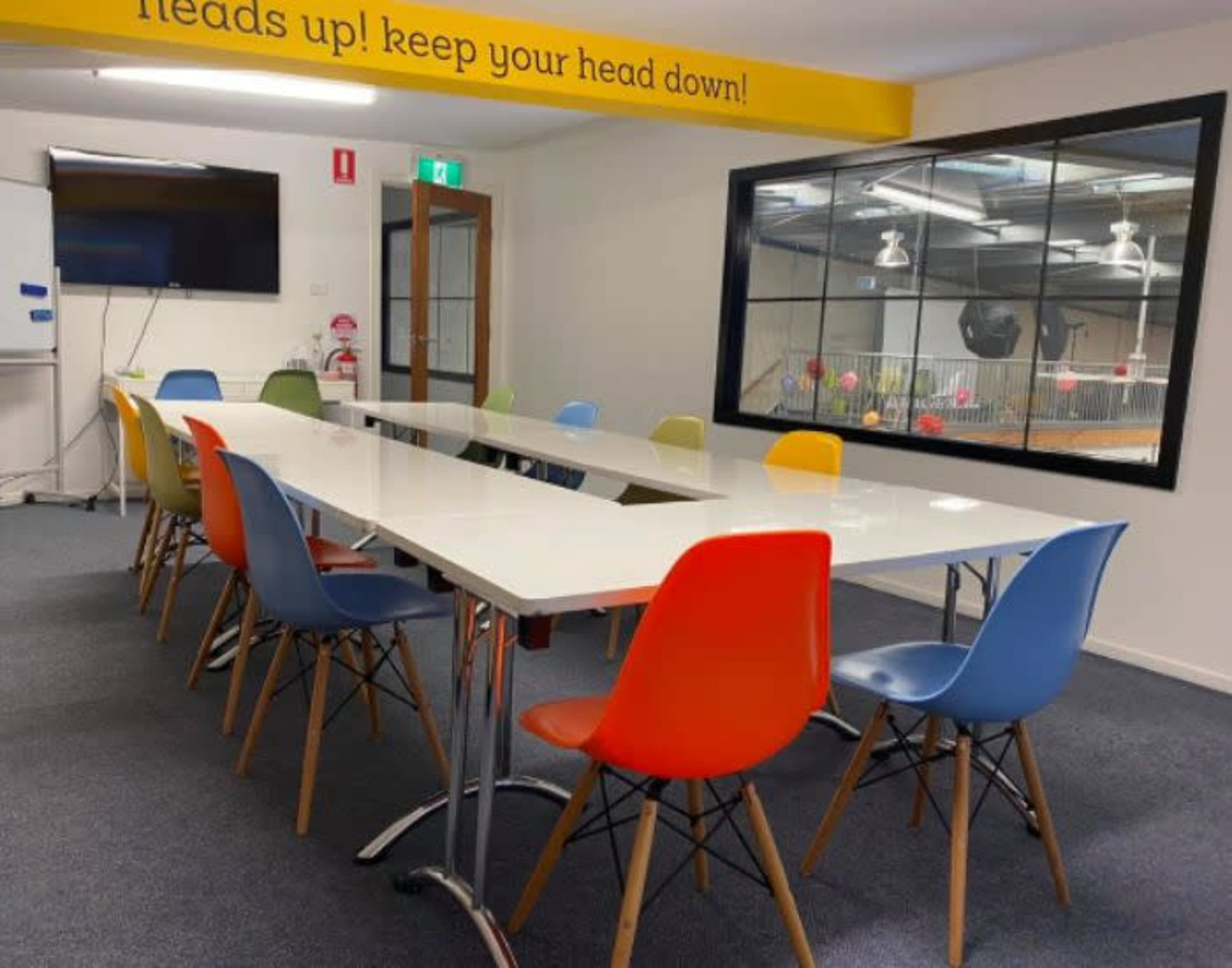 A modern conference room features a long white table surrounded by colorful chairs in orange, blue, and green.