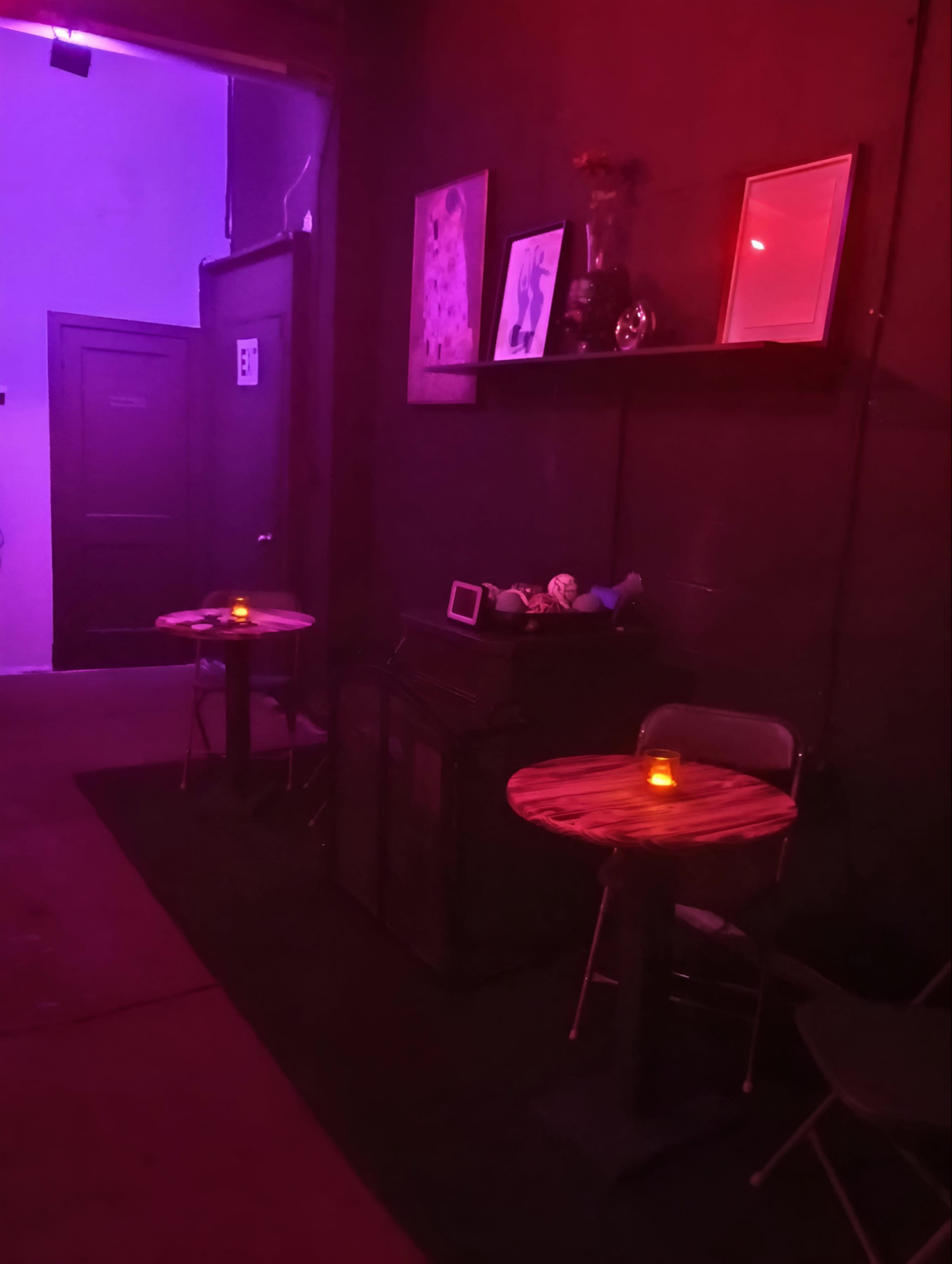 A dimly lit room with two small wooden tables, each with a candle, against a backdrop of purple and red lighting.