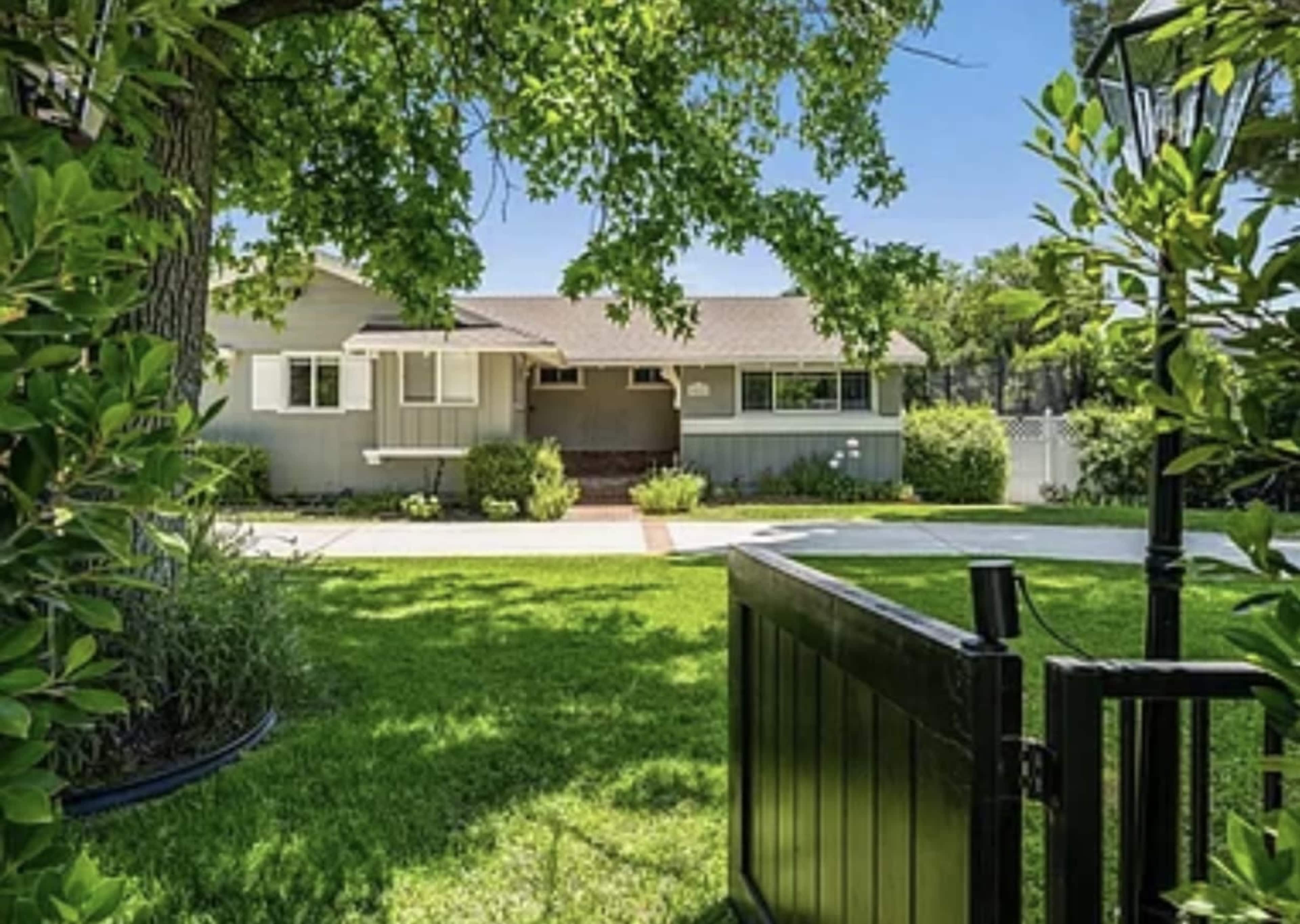 A well-maintained house is visible through a neatly landscaped yard with a grassy area and trees.