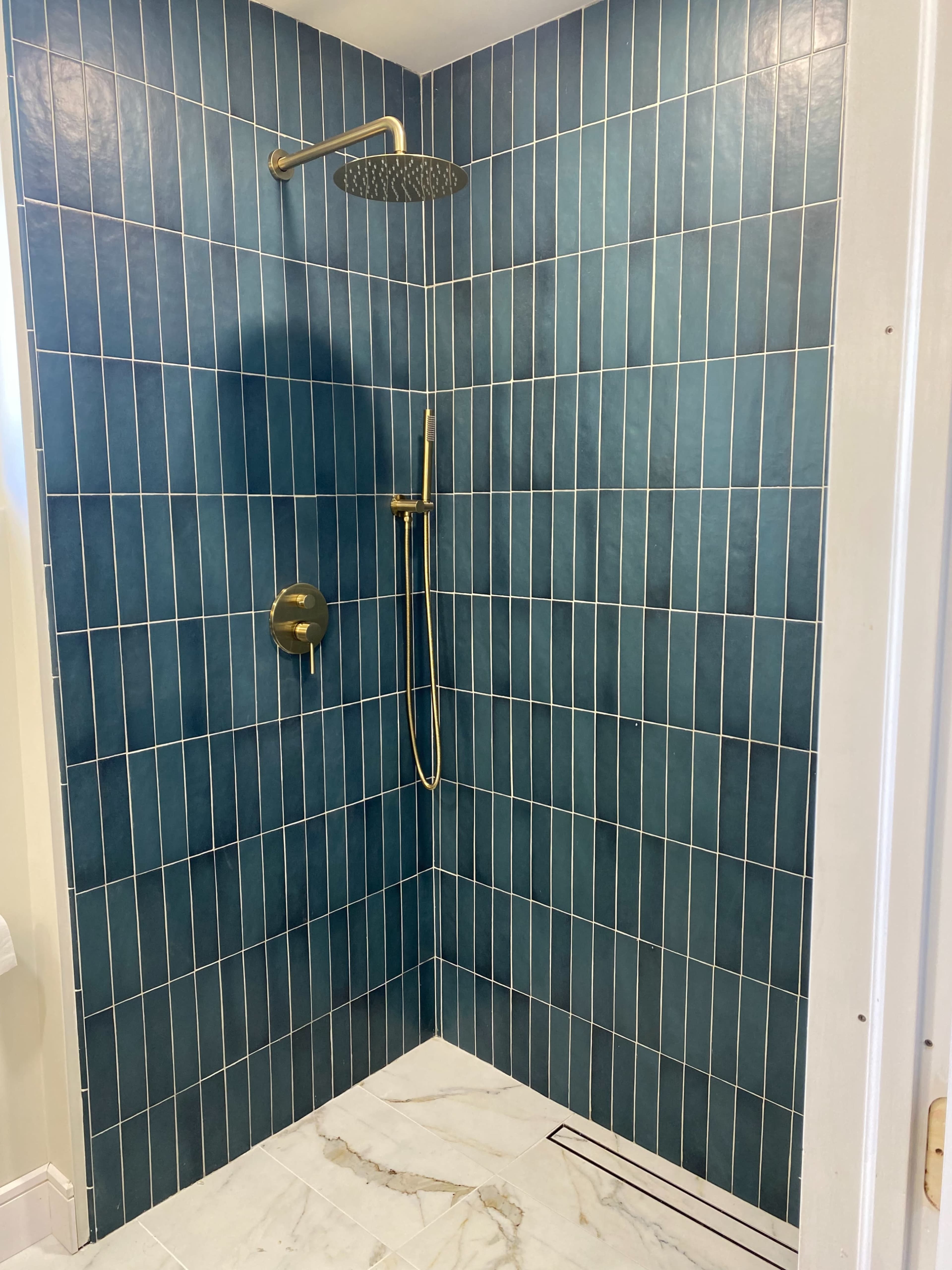A shower area with blue tiled walls and a gold showerhead and faucet.