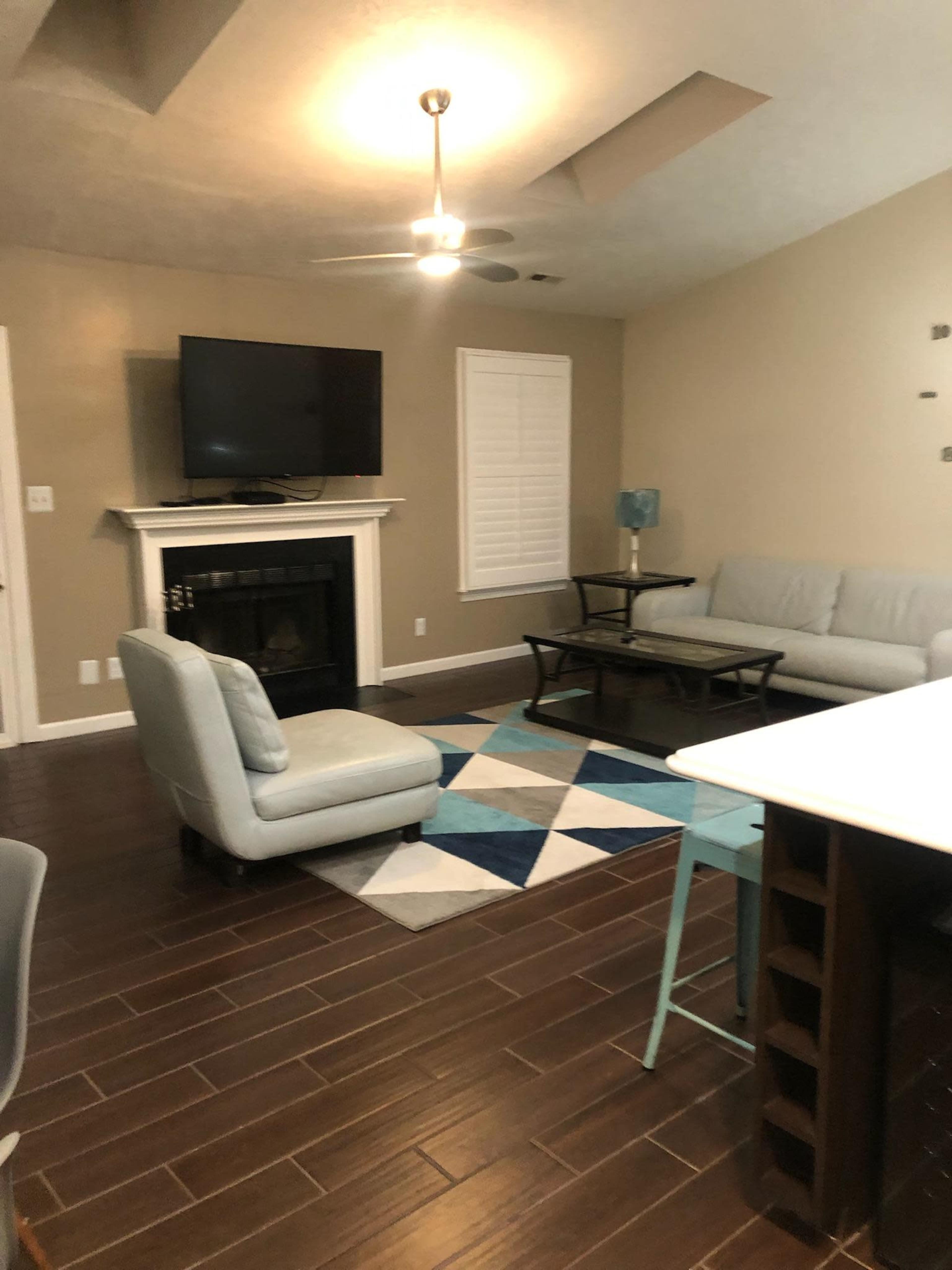 The room features a contemporary living space with a seating area, a television on the wall, and a patterned area rug.