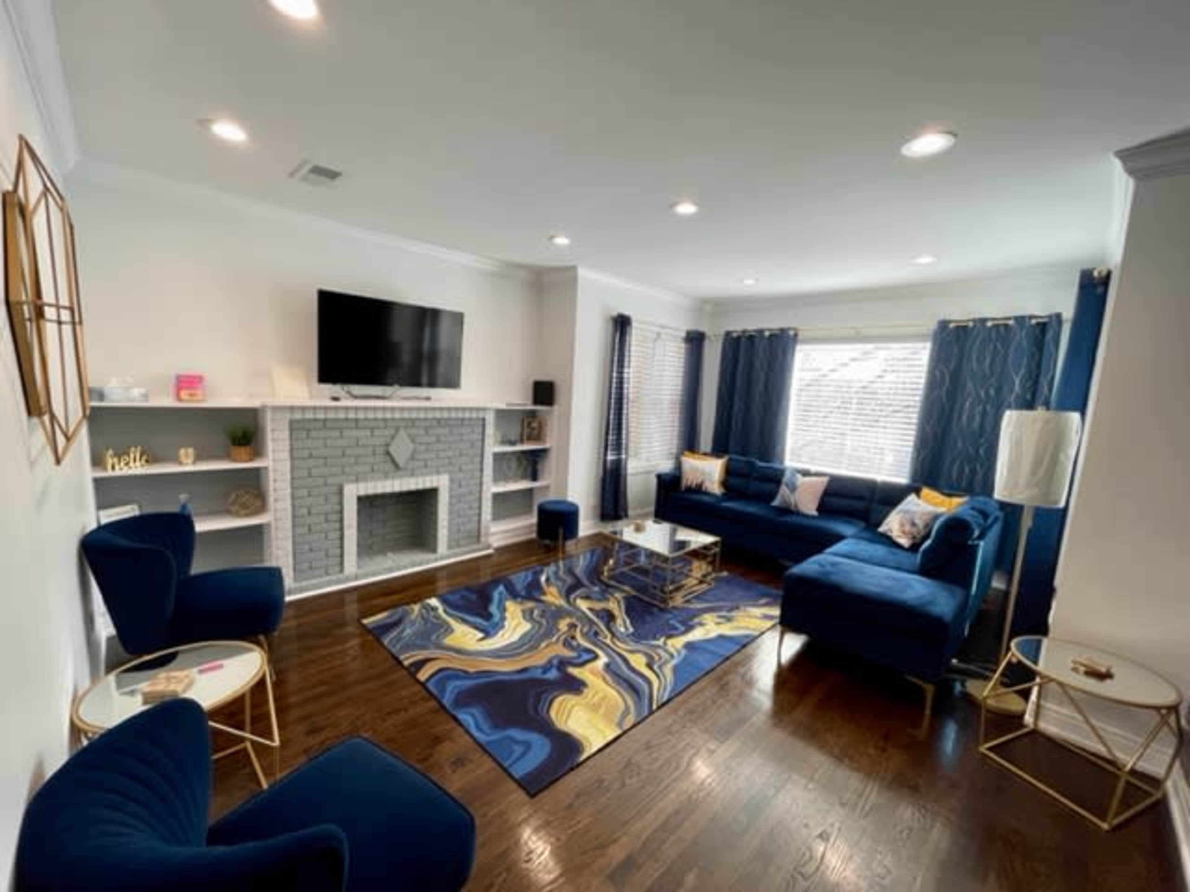The living room features a blue sectional sofa, a marble fireplace, and a dark wood floor, with a large rug and a TV mounted on the wall.