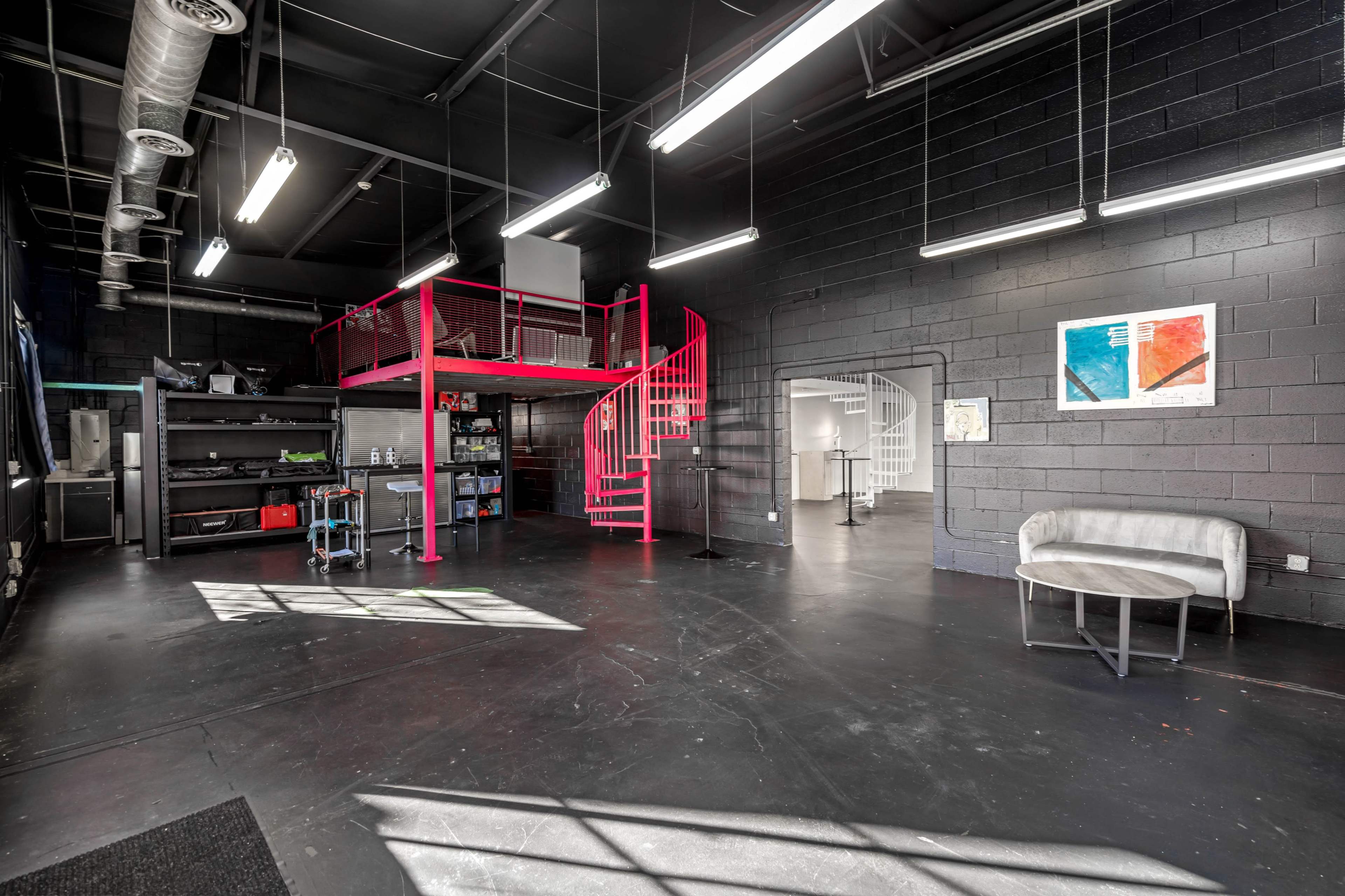 An industrial-style interior space featuring a spiral staircase, black walls, and various workstations.