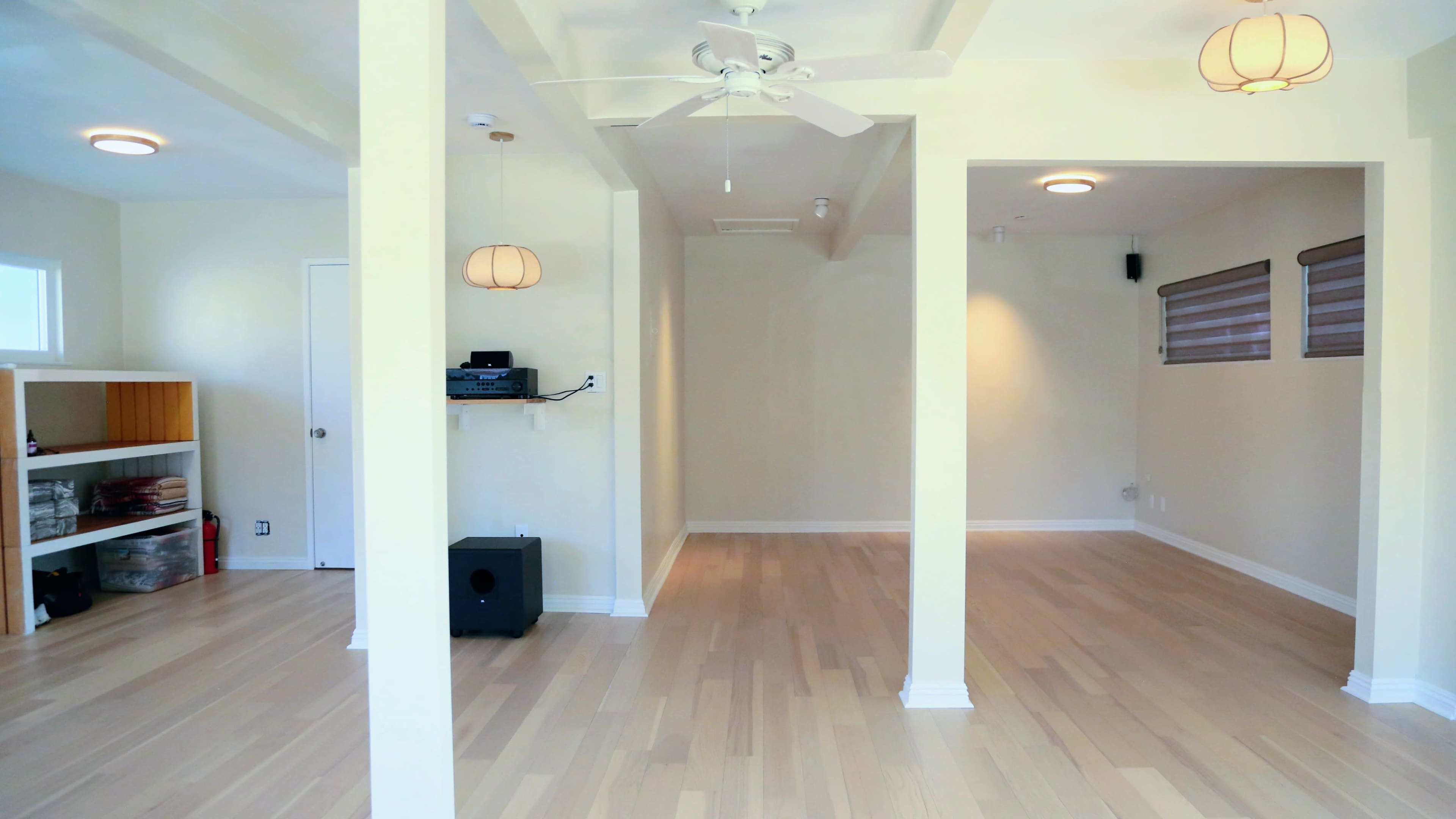 The image shows an empty room featuring light-colored hardwood flooring, ceiling fans, and two open doorways leading to adjacent spaces.