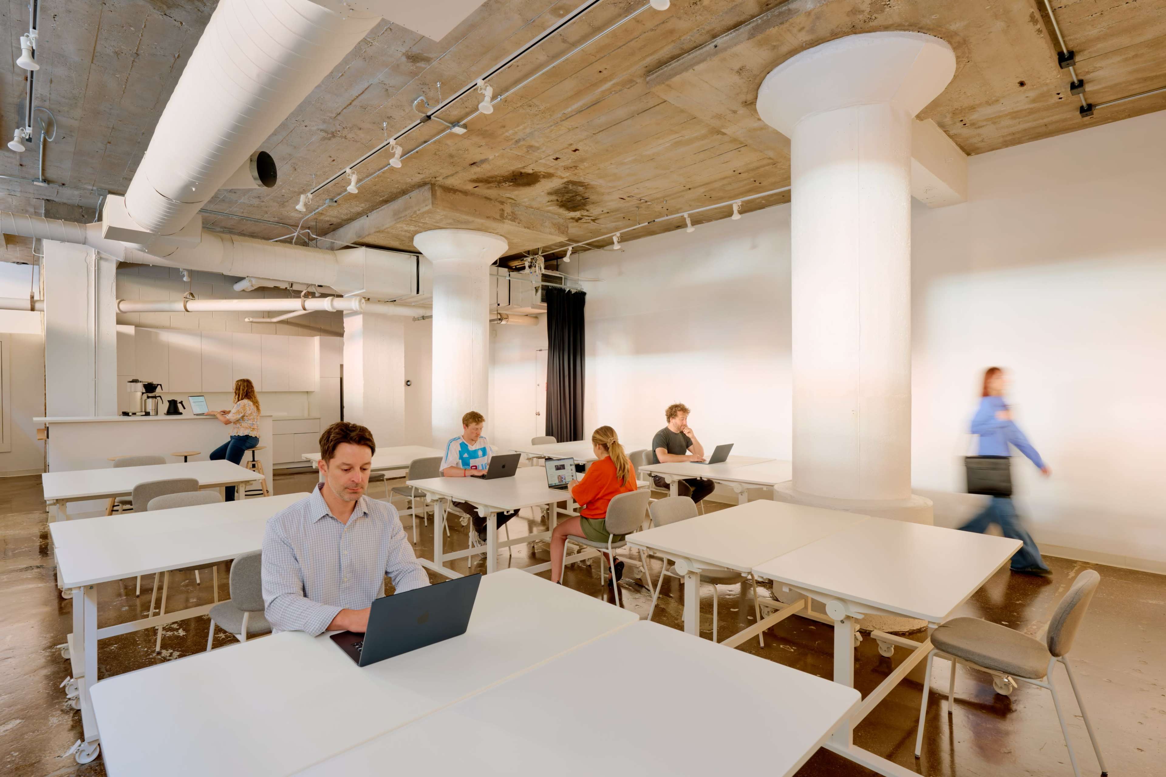 A spacious, modern office with several people working at tables while one person walks past.
