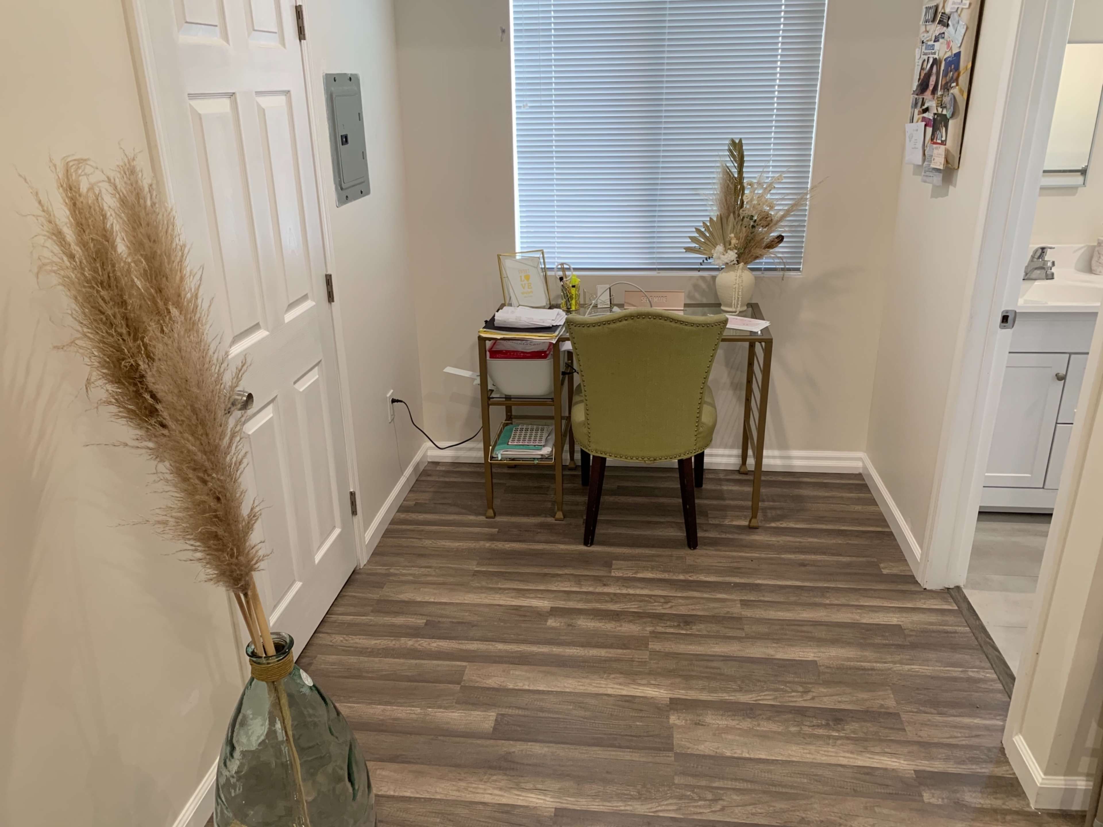 The image shows a small home office with a desk, chair, and decorative plants, located next to a door and a bathroom entrance.