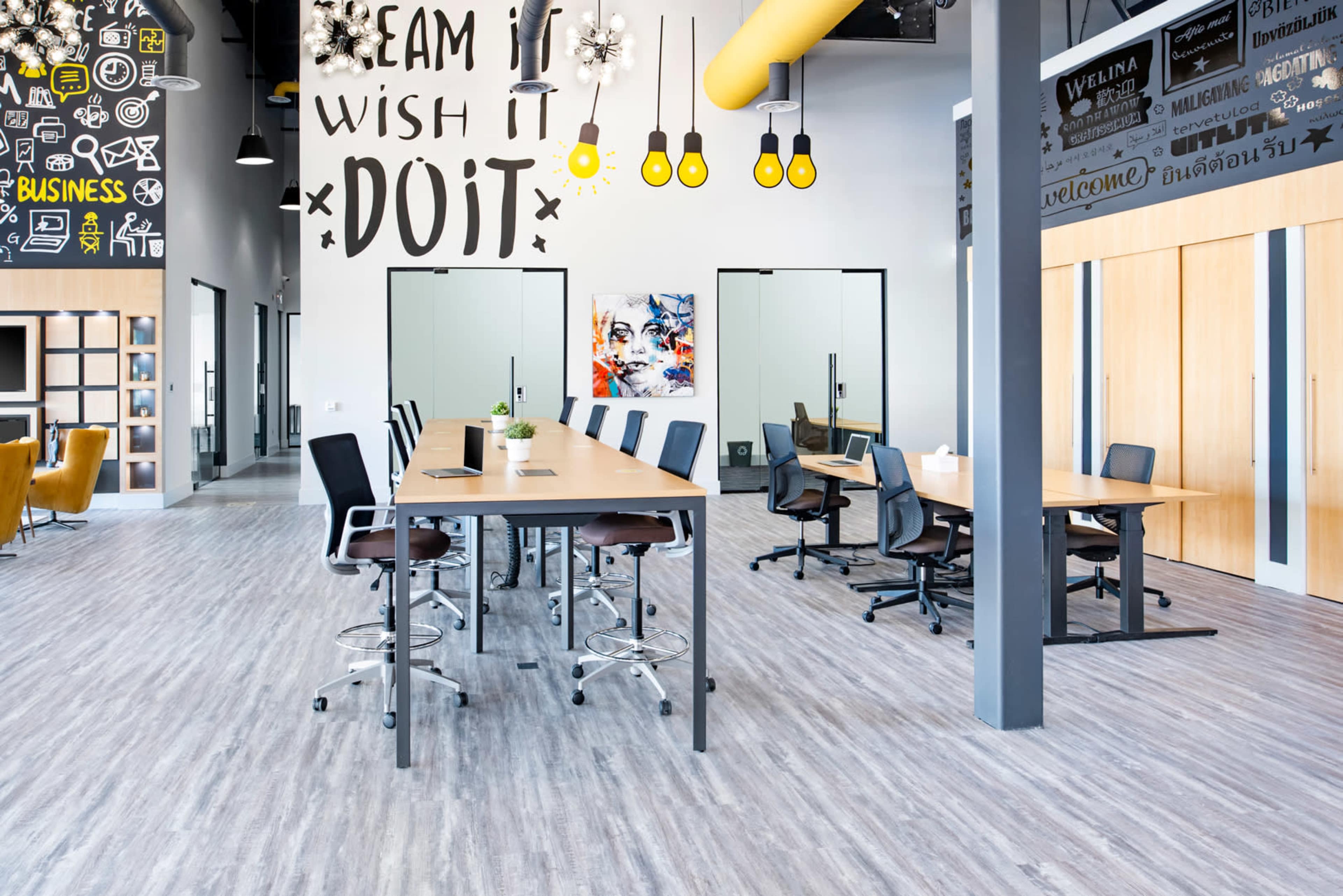 A modern office space with multiple desks, chairs, and glass meeting rooms, decorated with inspirational wall art.