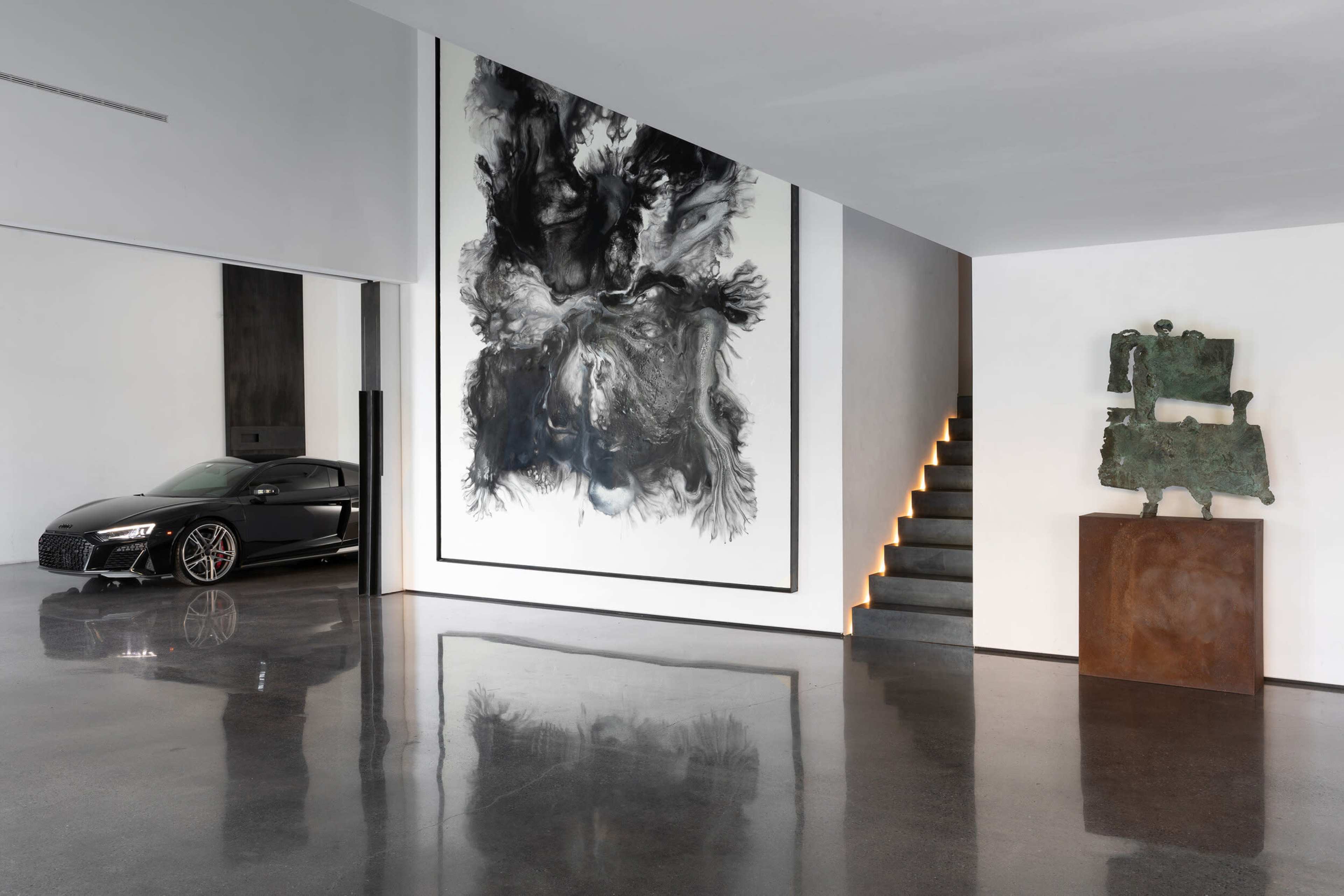 A modern interior space featuring a black car, a large abstract artwork on the wall, a sculpture, and a staircase with illuminated steps.