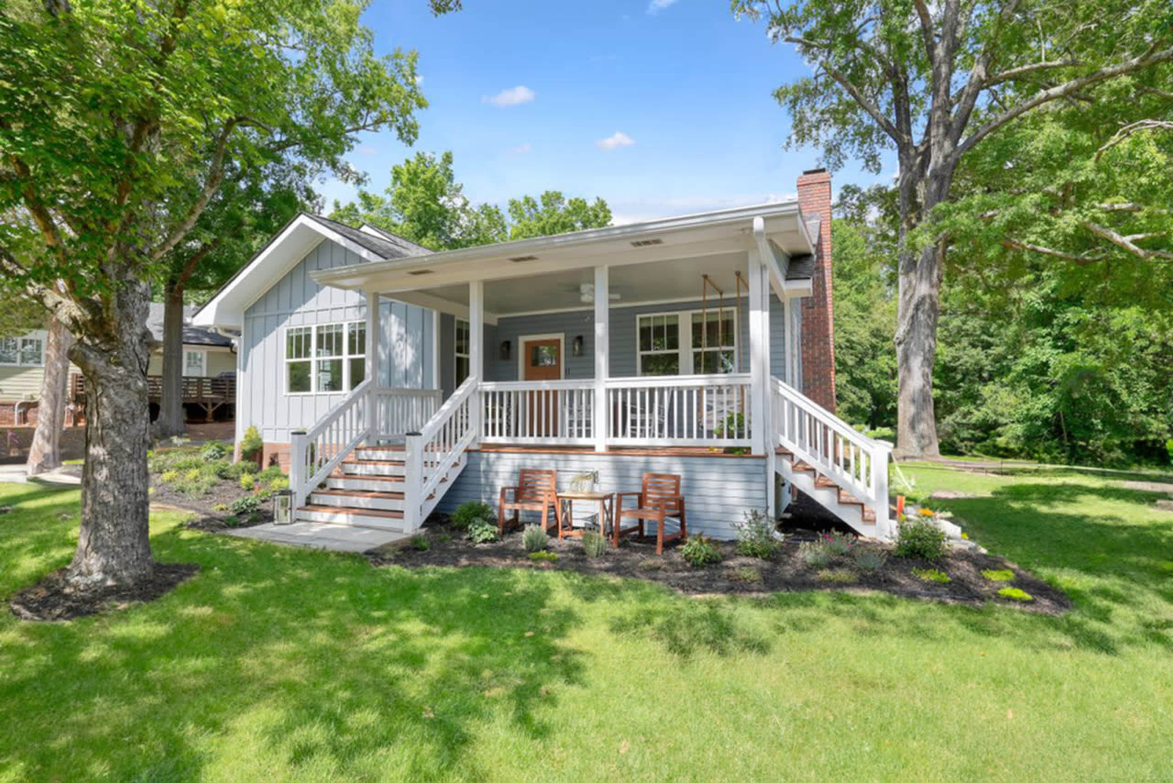 A single-story house with a front porch and steps is surrounded by a green lawn and trees.