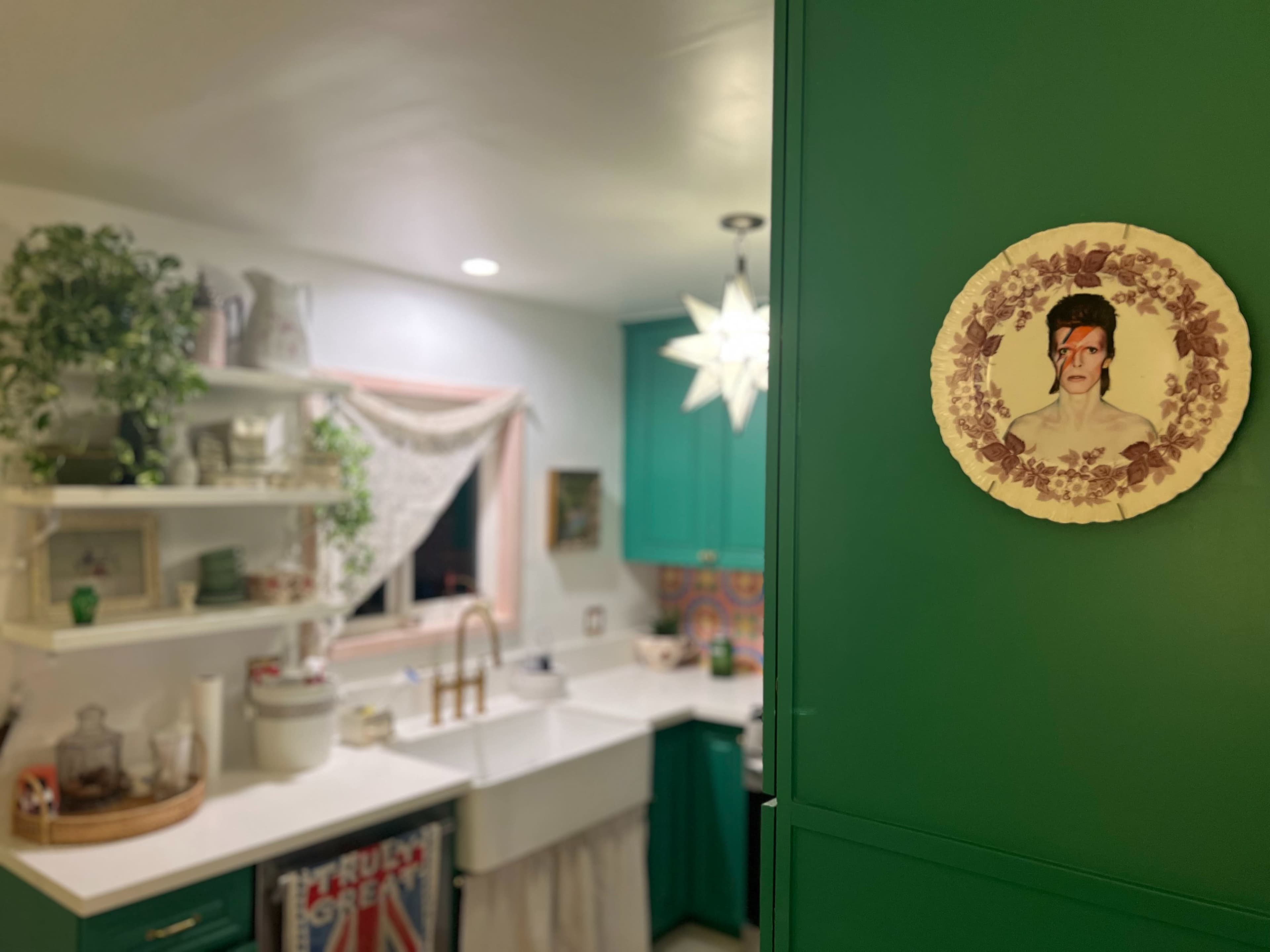 A vibrant kitchen features teal cabinetry, open shelves with decor, and a plate depicting a portrait on the wall.