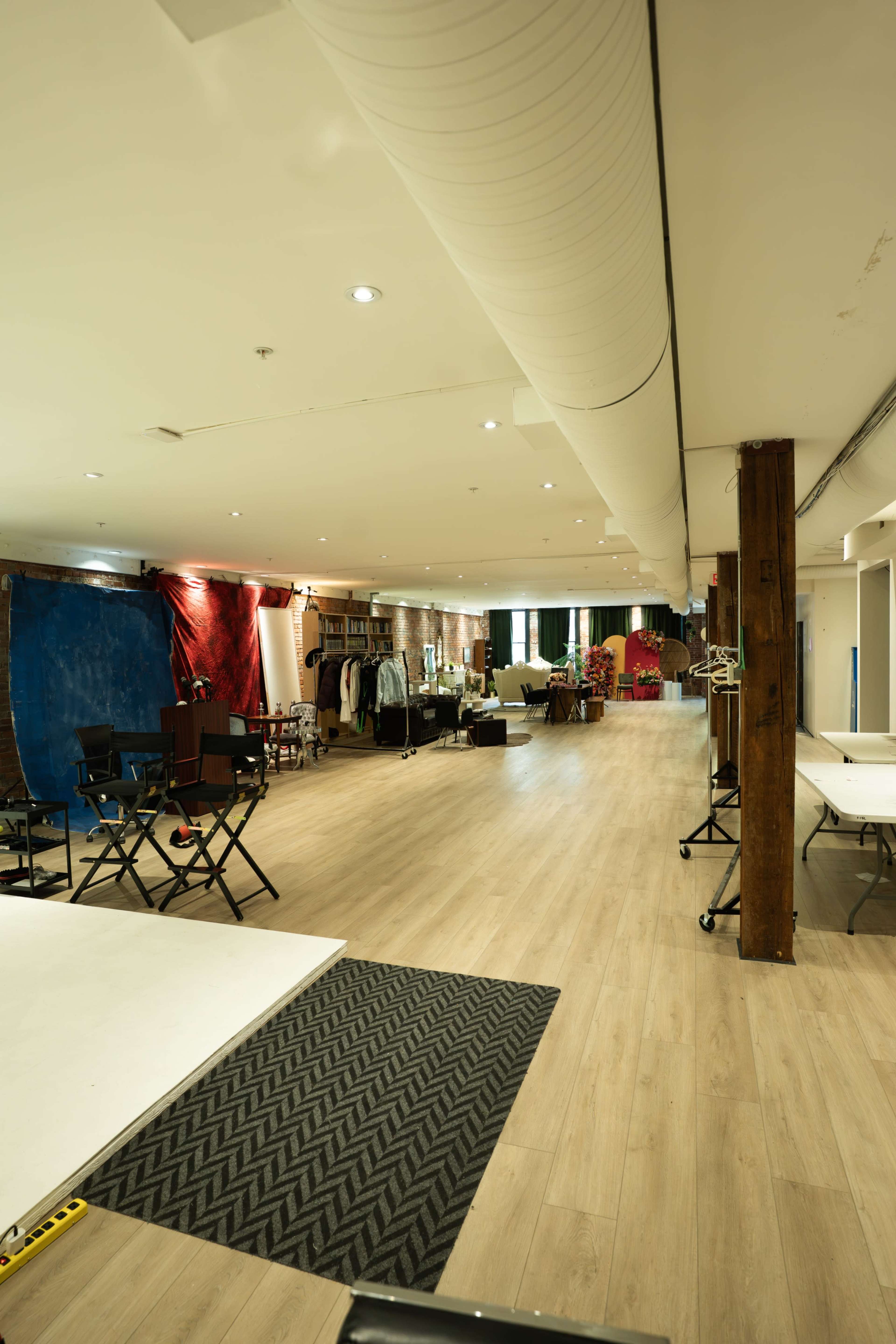 The image shows a spacious studio interior with wooden flooring, featuring various equipment and furniture arranged along the walls.