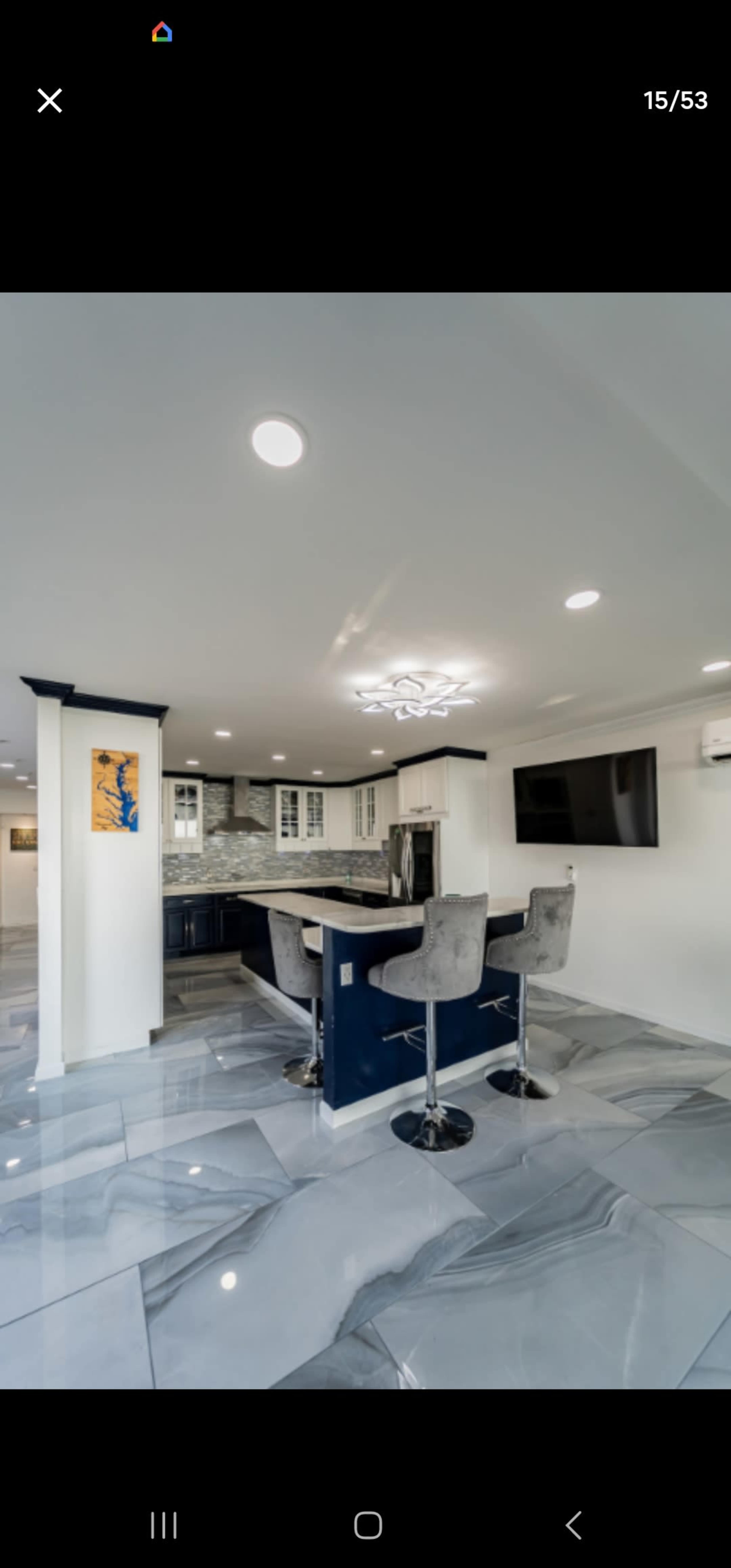 A modern kitchen features a large island with barstools, polished gray tiles, and contemporary appliances.