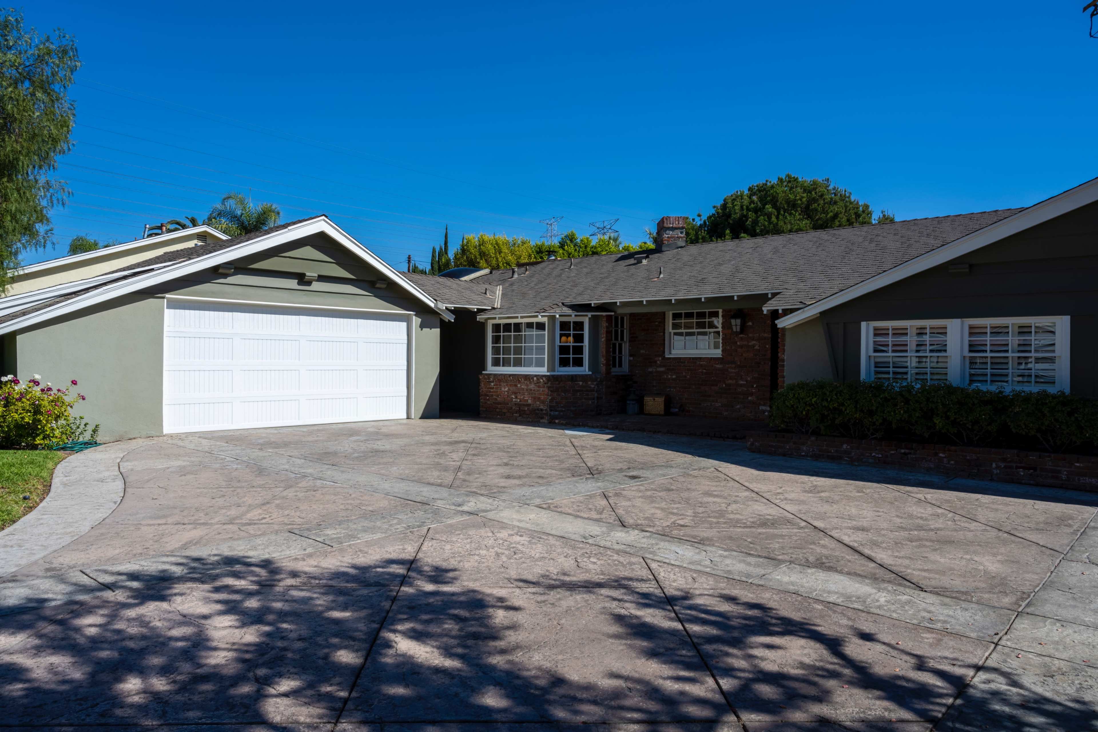 A single-story house with a two-car garage and a concrete driveway under a clear blue sky.