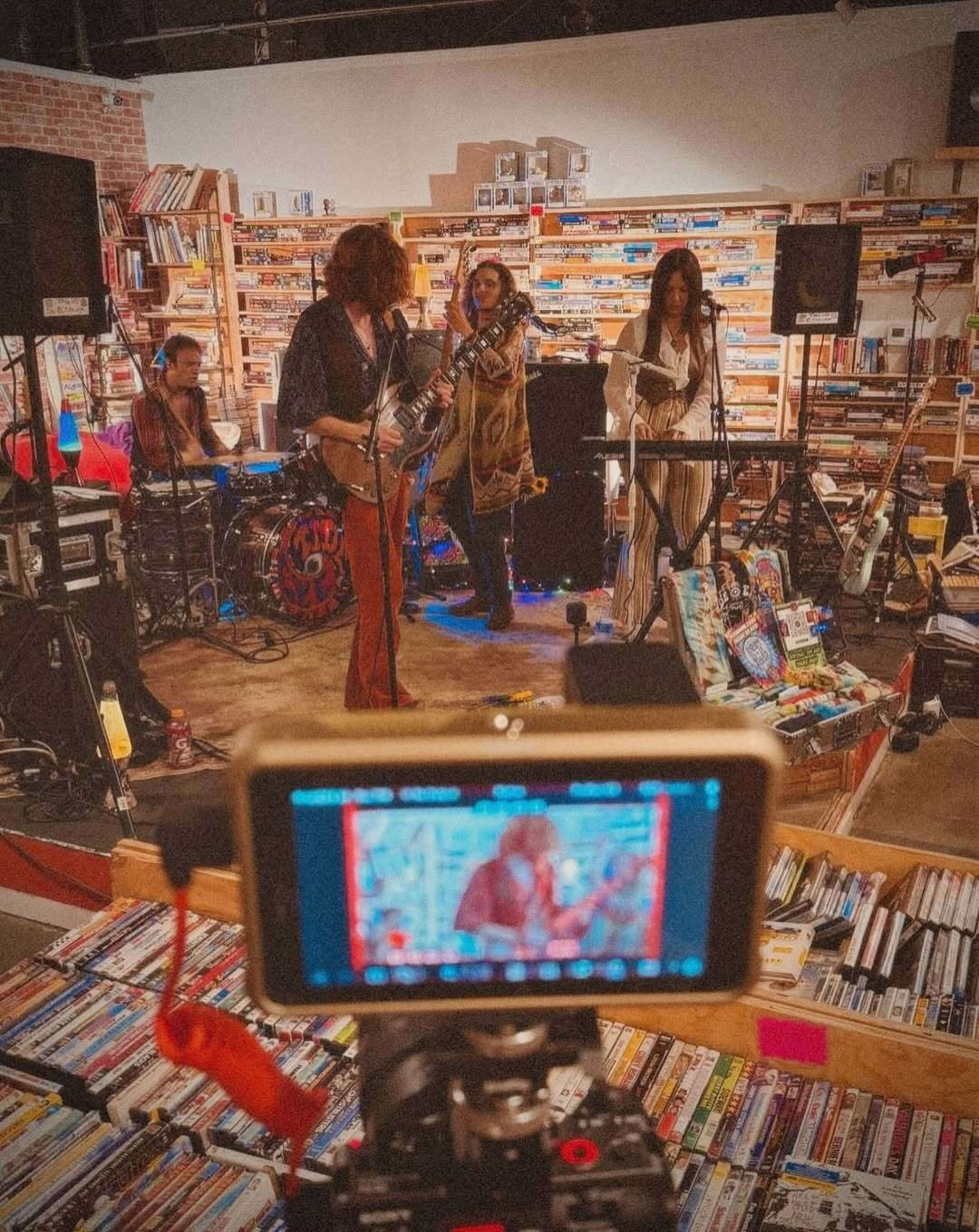 A band performs on a small stage in a bookstore, surrounded by shelves filled with books and DVDs.