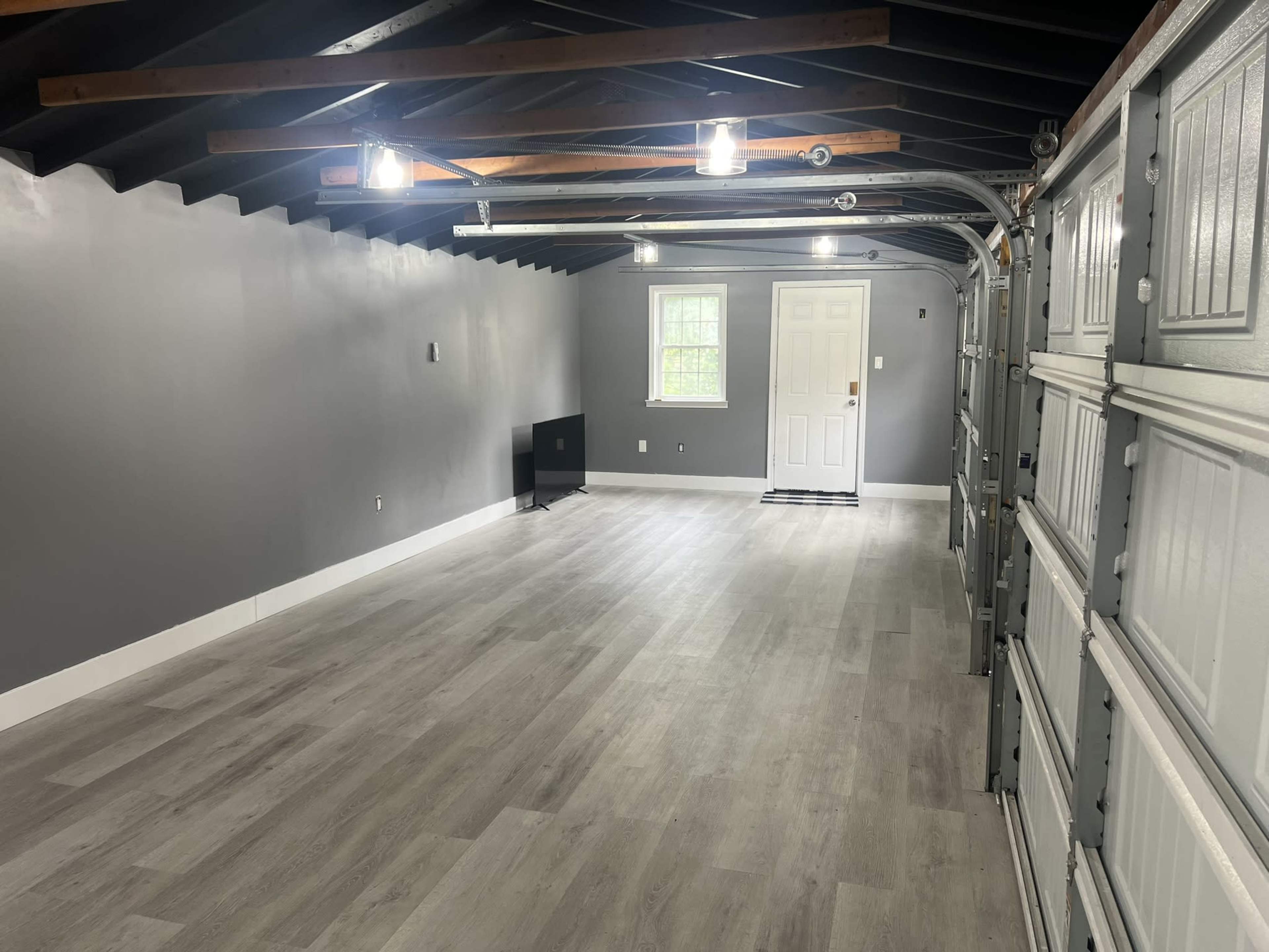 A spacious, grey-walled garage with a smooth floor, overhead lighting, and a door leading outside.