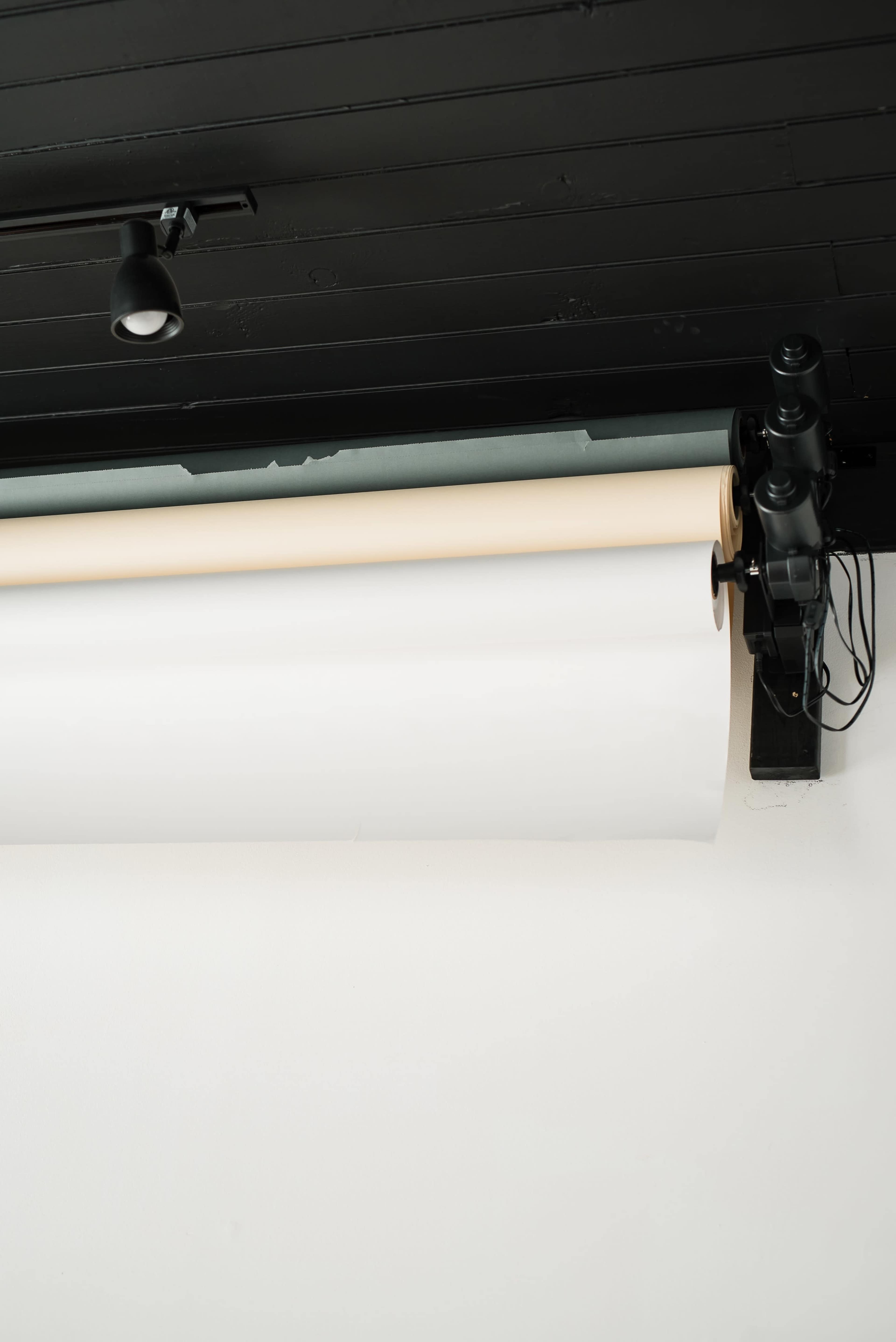 A roll of white paper is mounted on a black ceiling, with a spotlight above it.