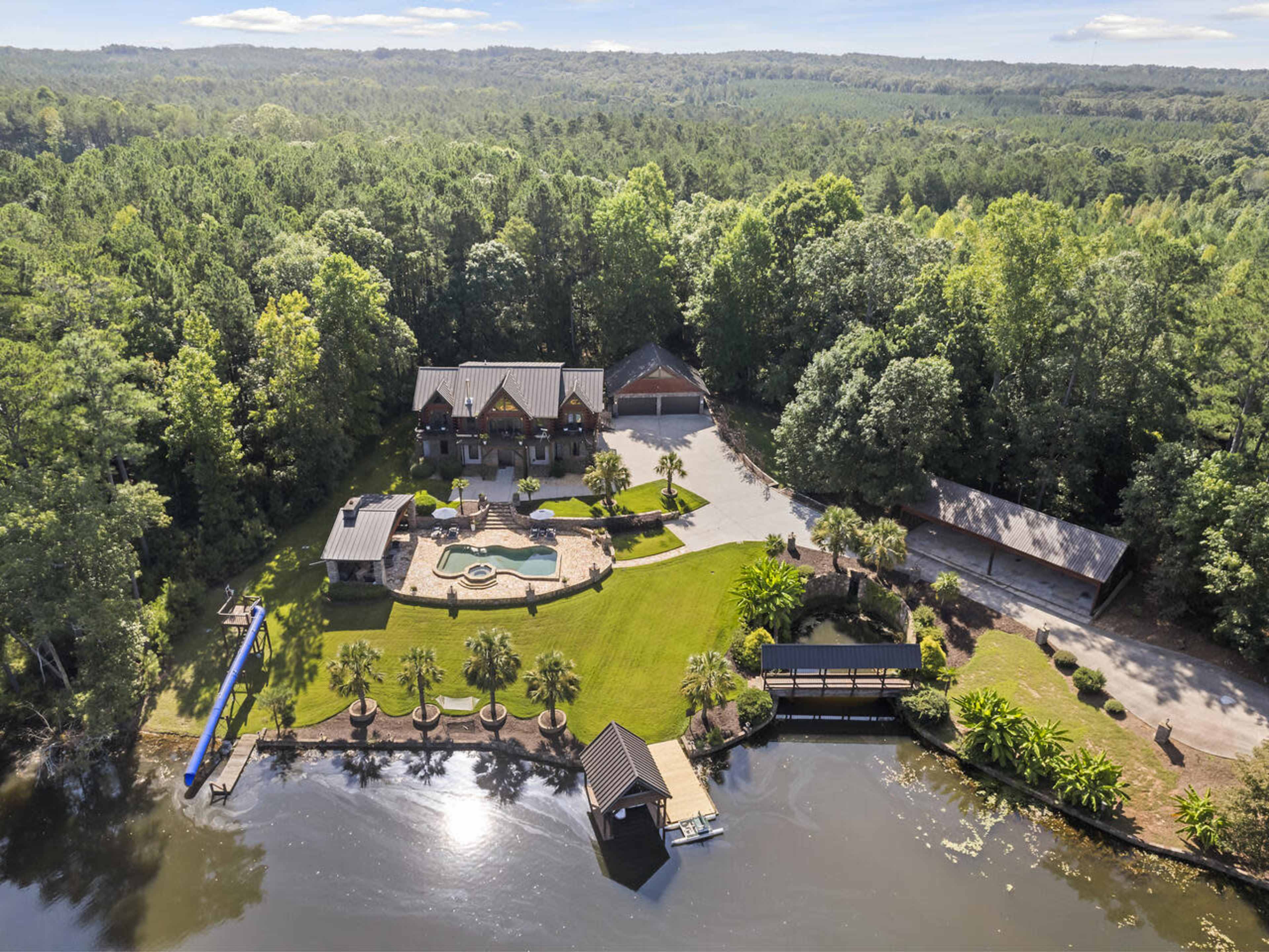 A large house with a swimming pool and landscaped grounds situated near a body of water and surrounded by trees.