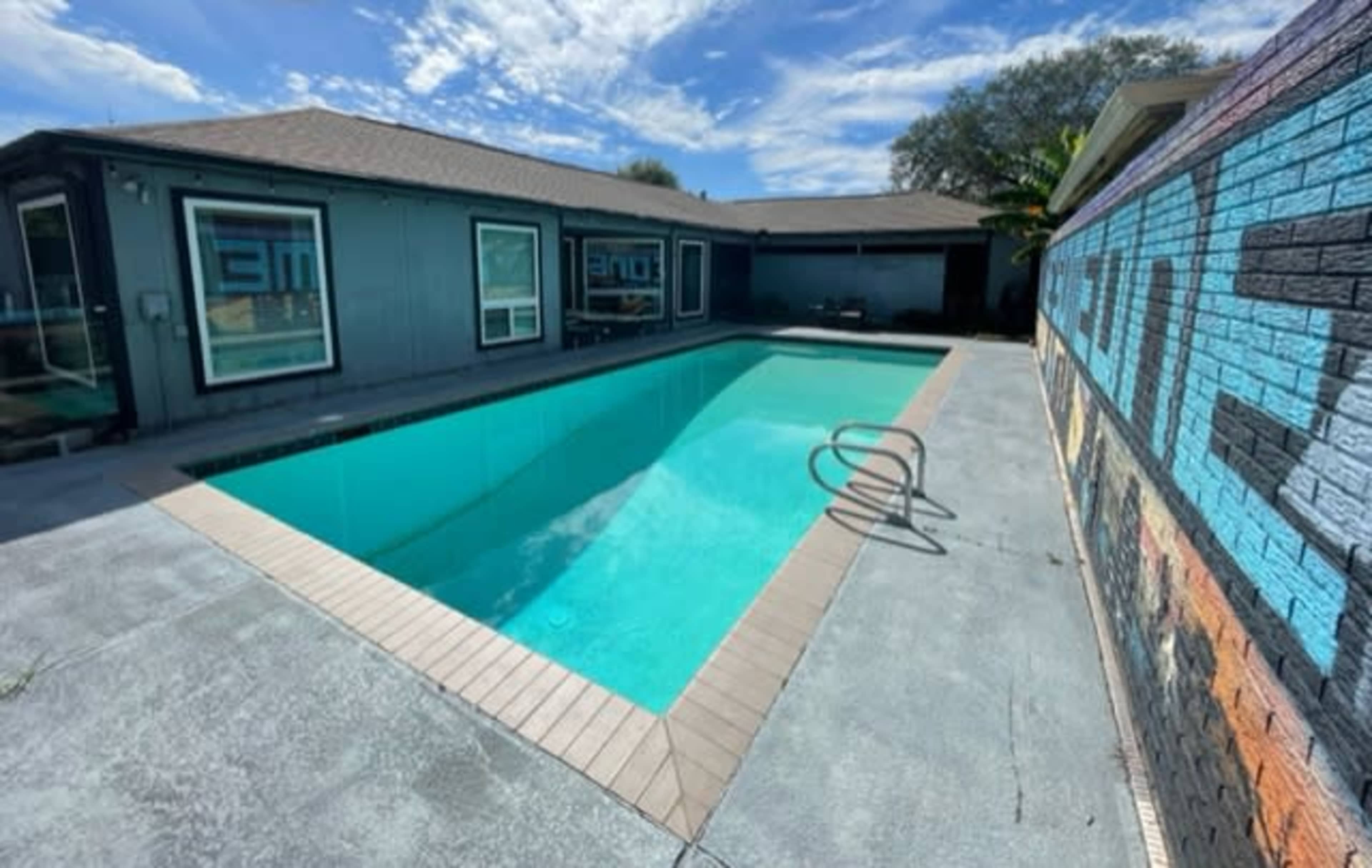 A swimming pool with a clear blue surface surrounded by a concrete deck and a wall featuring colorful graffiti.