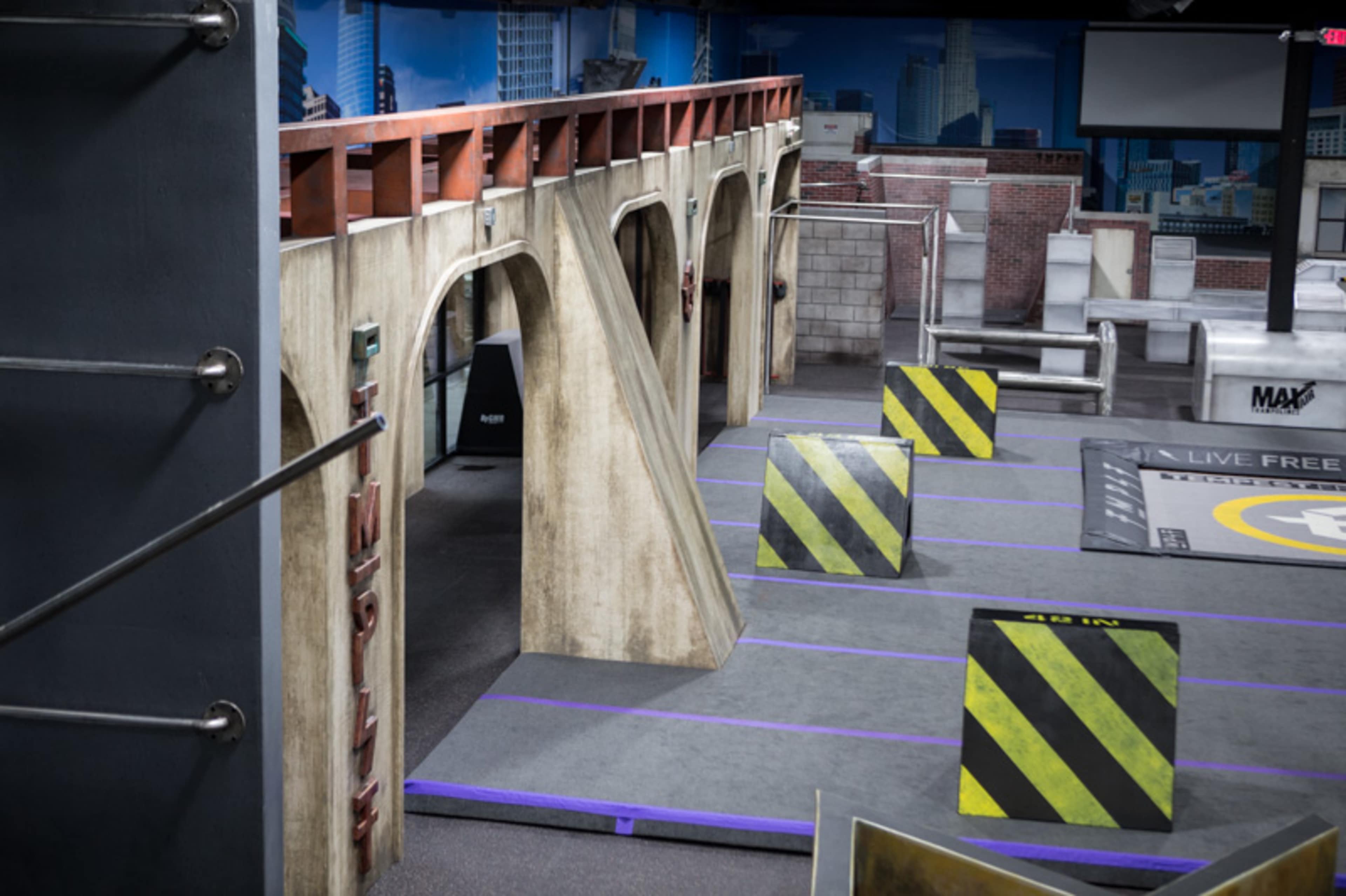 The image shows an indoor obstacle course featuring concrete-like structures and yellow-black striped barriers.