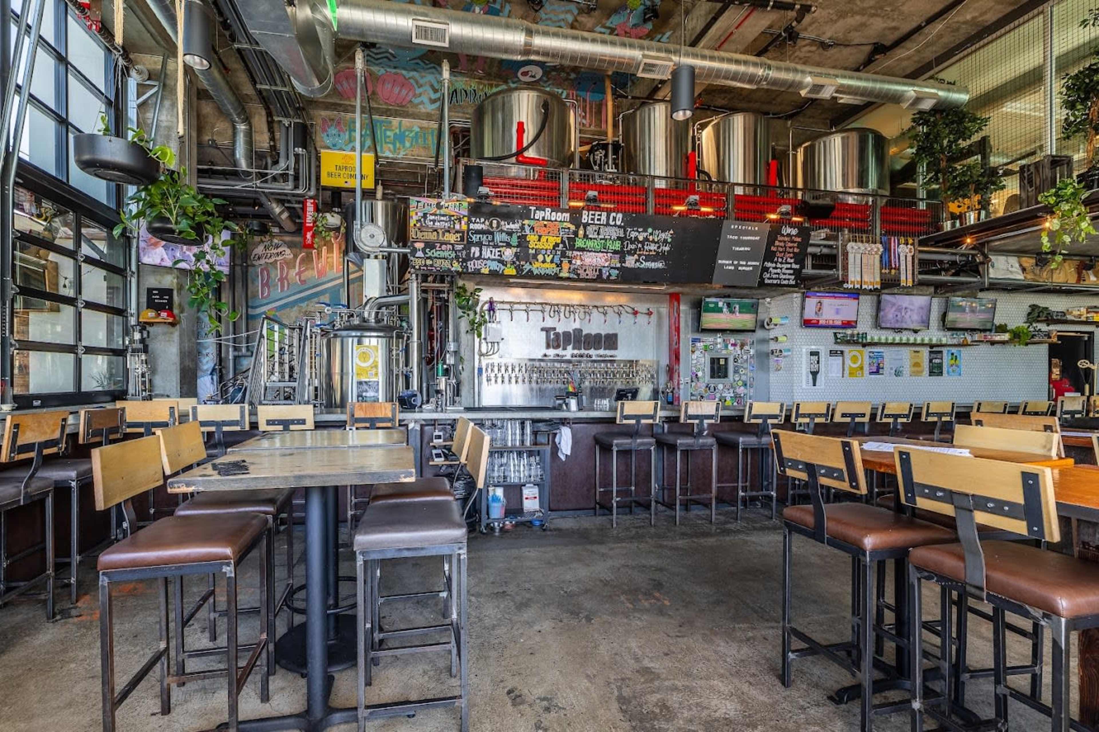 A spacious, industrial-style brewpub with metal brewing tanks, a long bar, and seating arranged at wooden tables.