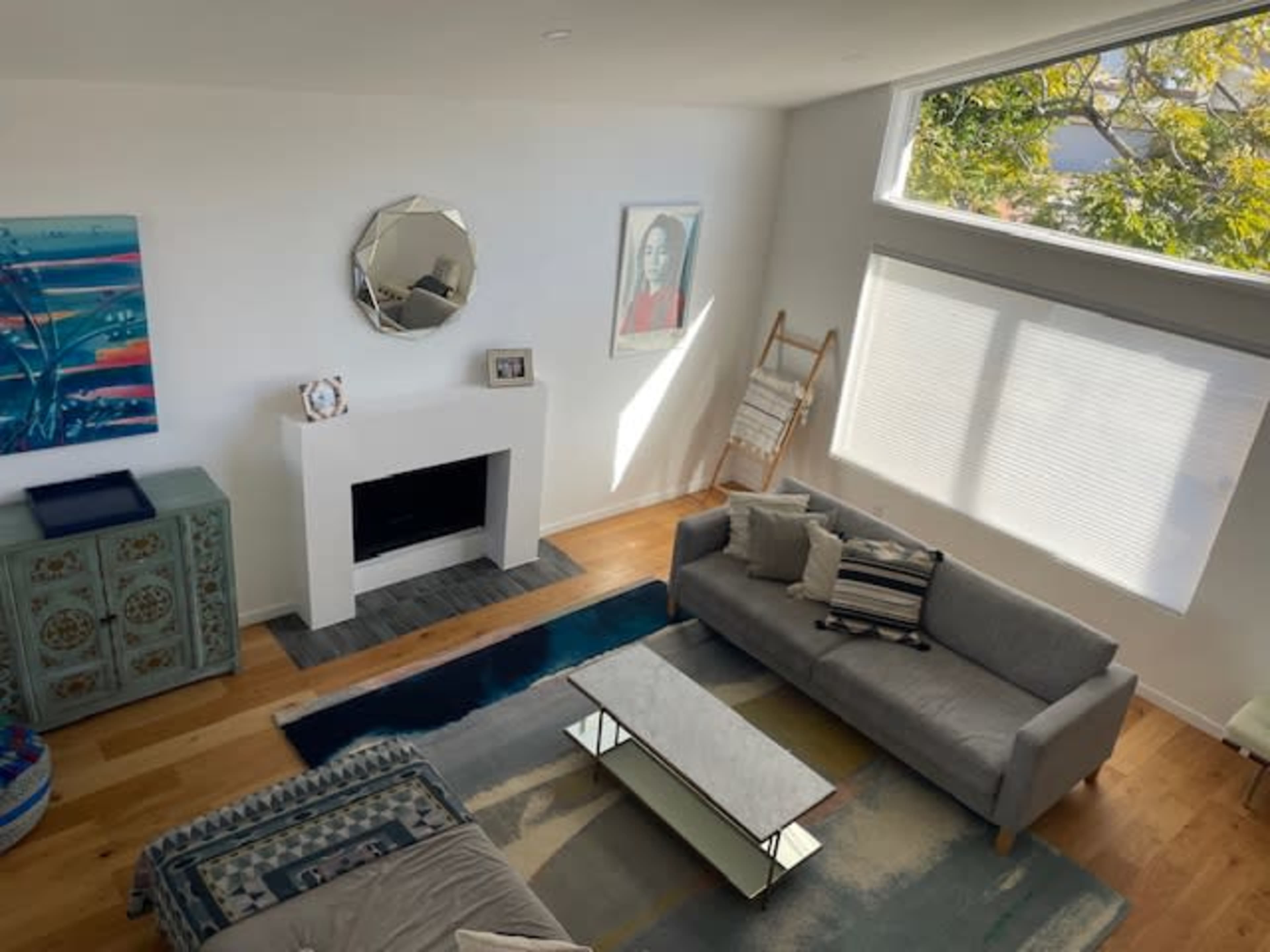 A modern living room features a gray sofa, a coffee table, a fireplace, and large windows with natural light.