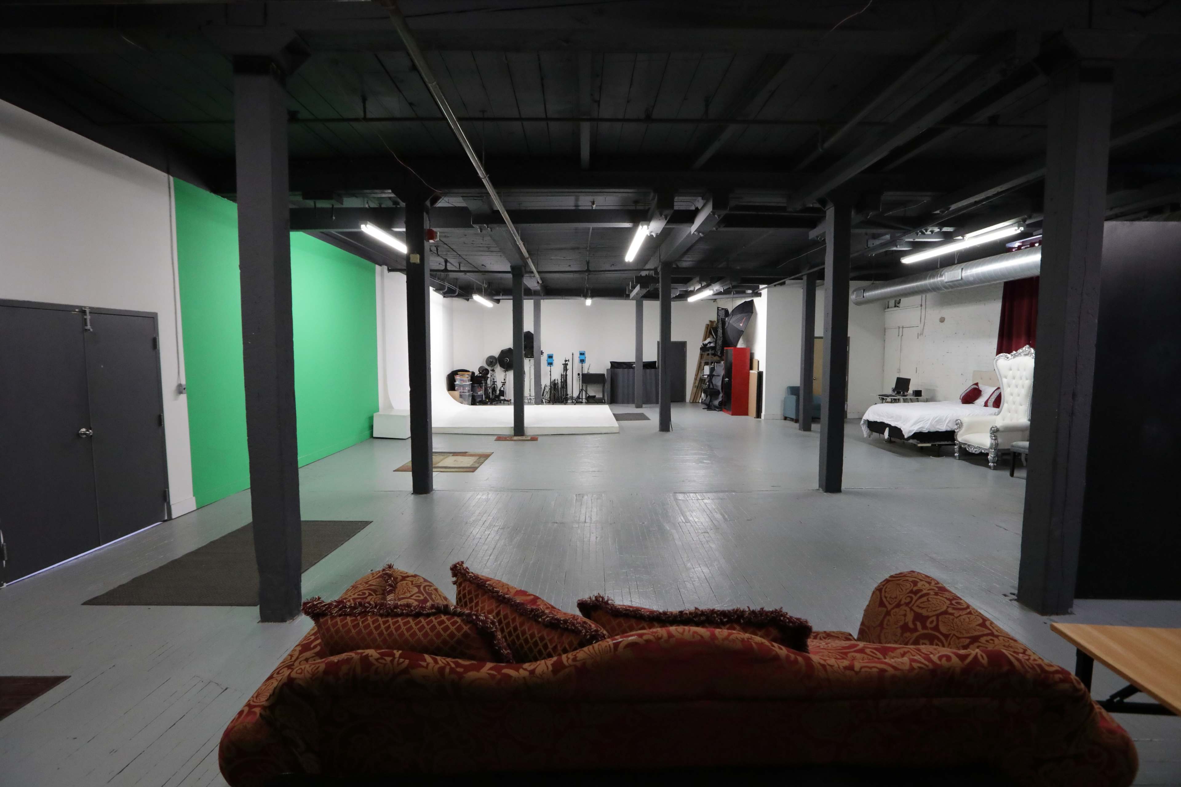 A large, open studio space with a green screen backdrop and various equipment along the walls, including a bed setup.