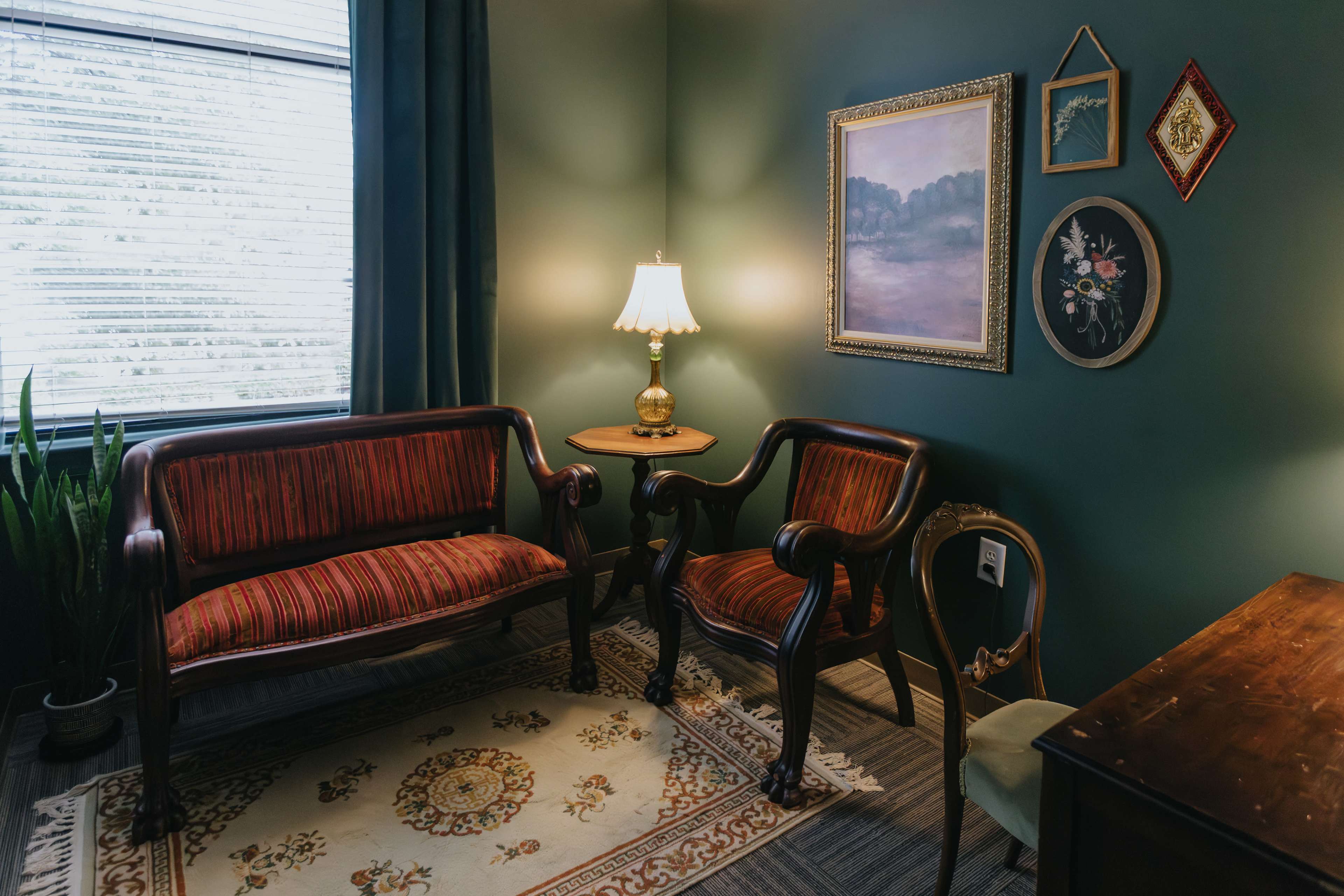 A cozy seating area features two vintage chairs, a small side table with a lamp, and wall art in a green room.