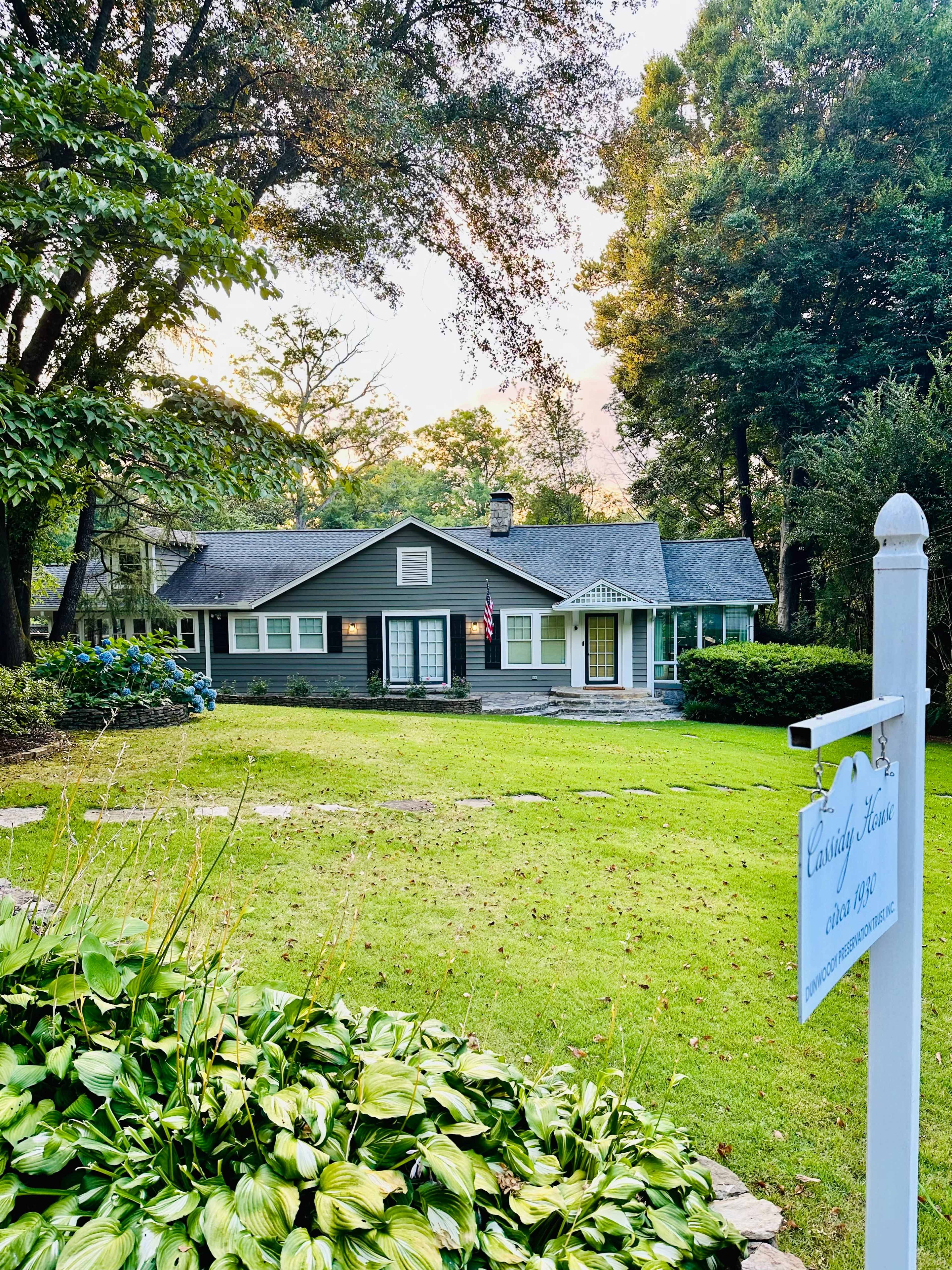 A single-story gray house with an American flag in front is surrounded by a well-maintained lawn and trees.