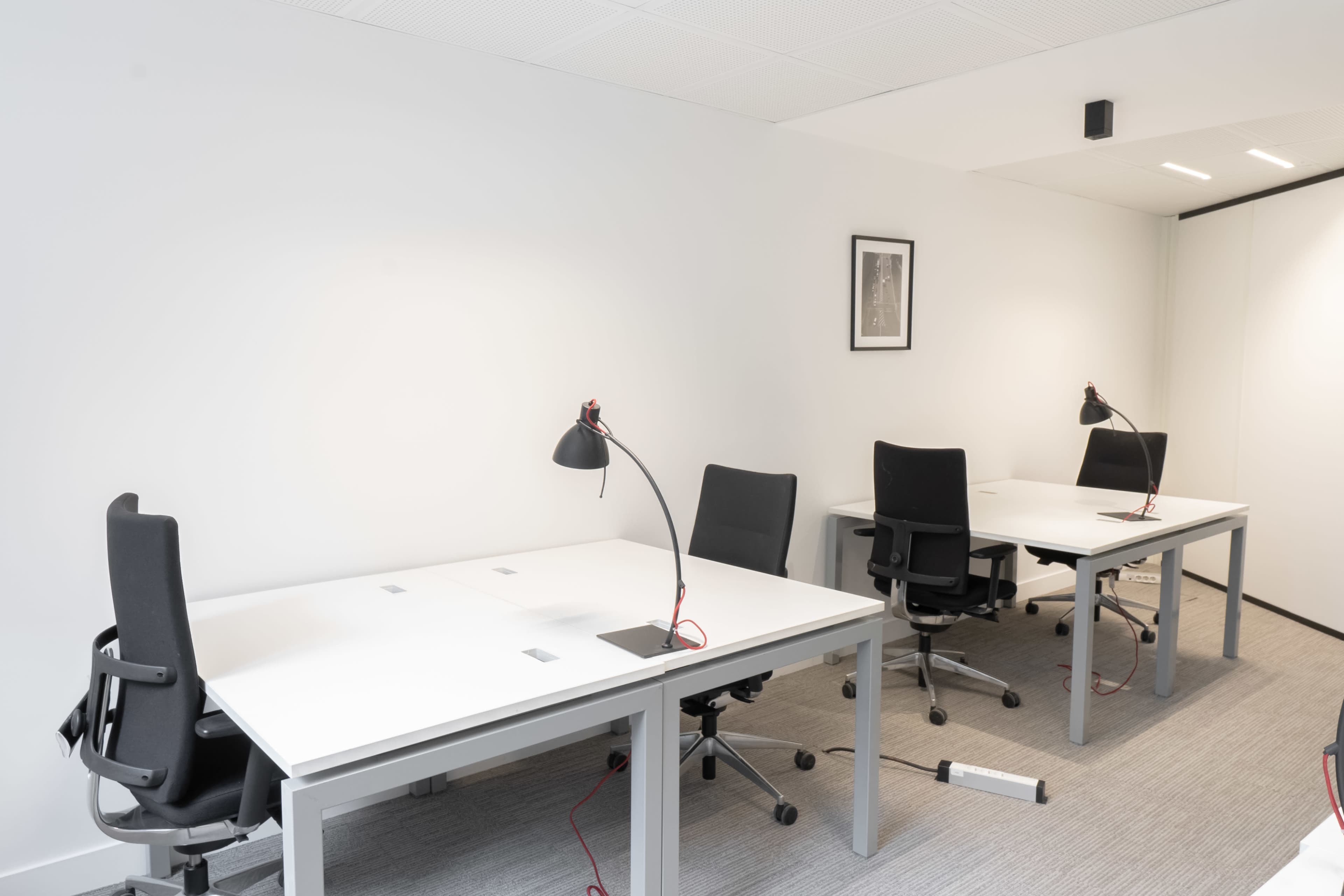 The image shows a modern office space with three workstations, each equipped with a desk lamp, black office chairs, and minimal wall decor.