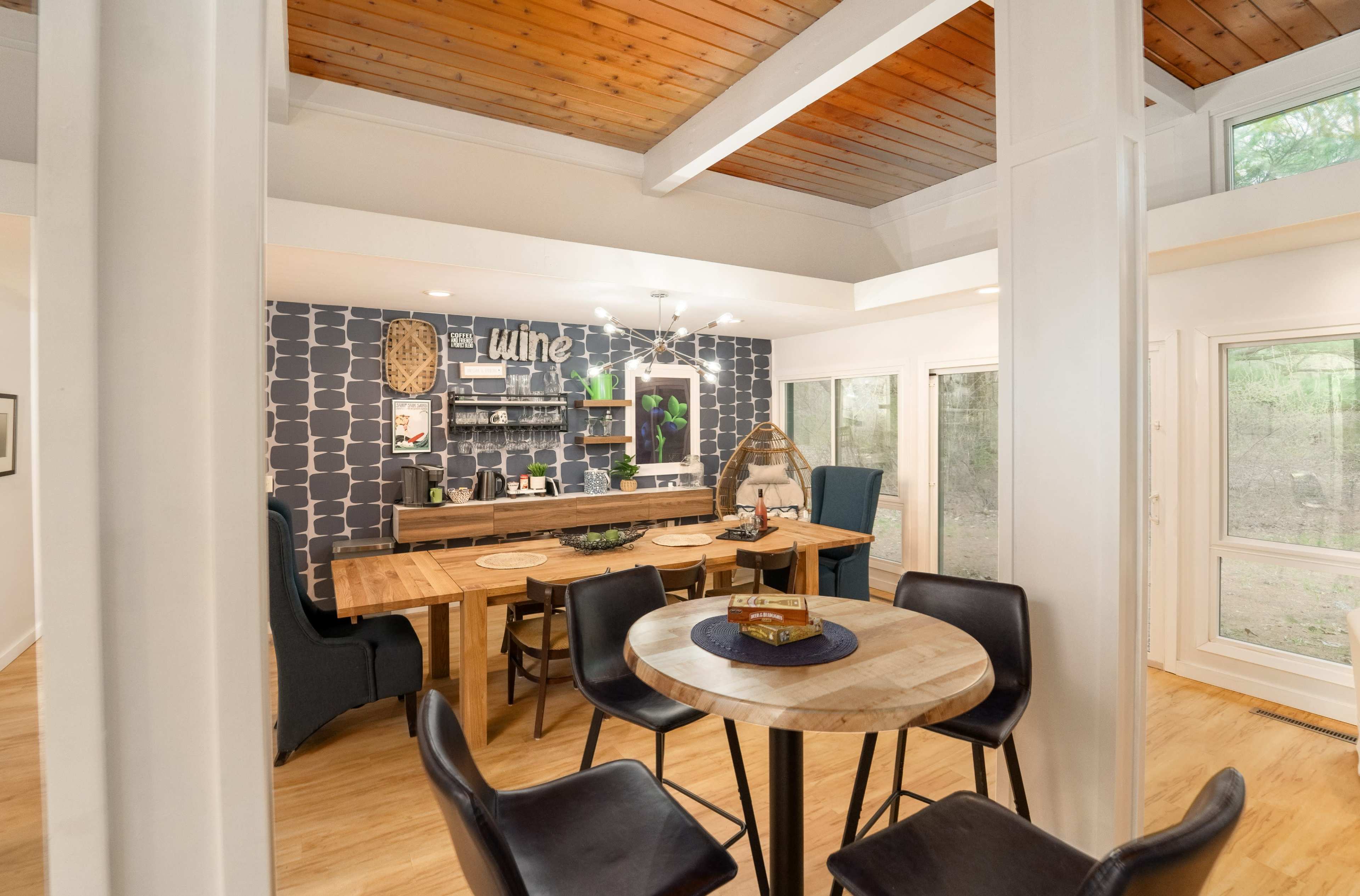 A modern dining area with a wooden table surrounded by chairs, a patterned accent wall, and large windows providing natural light.