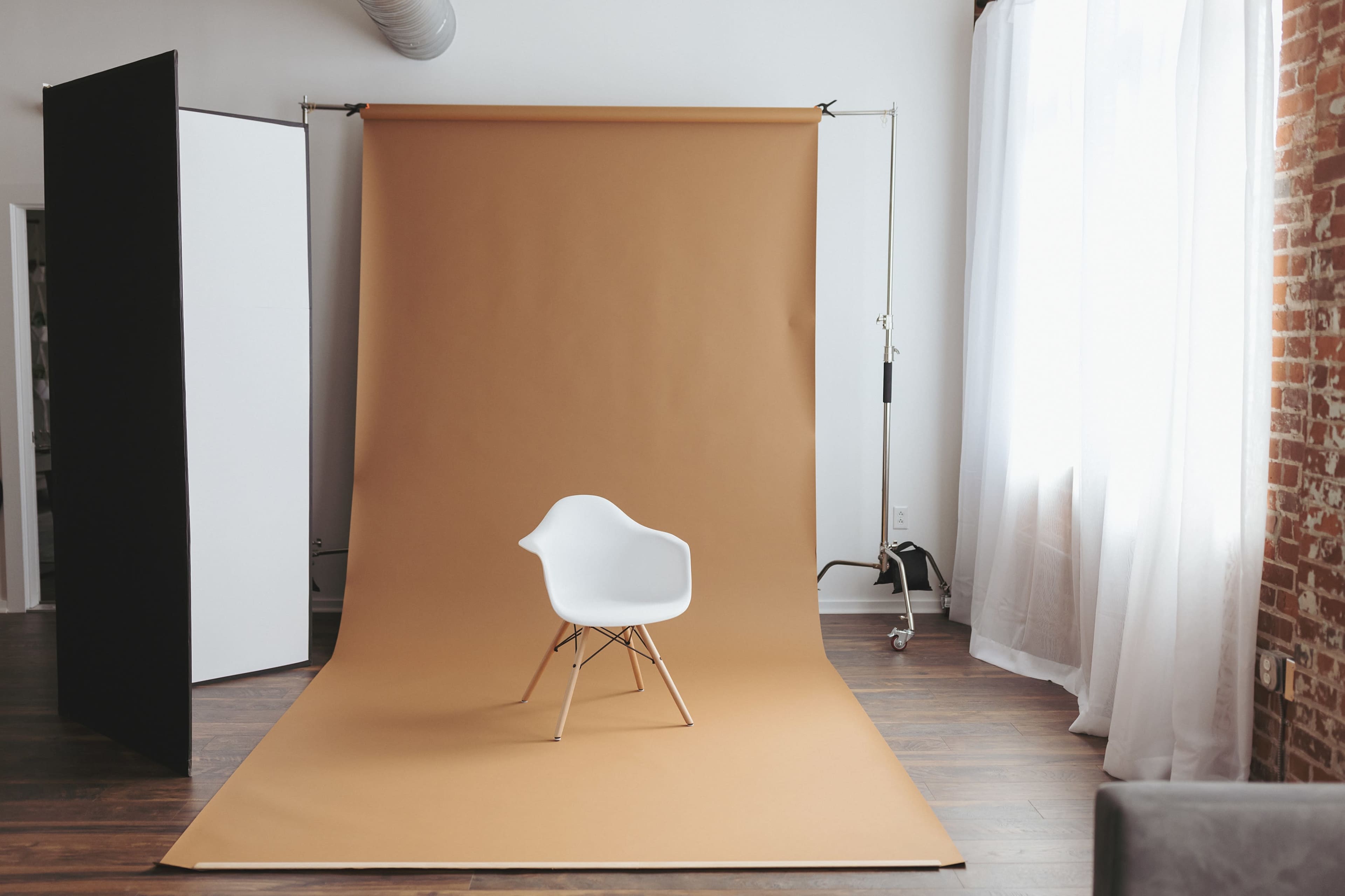 A white chair sits on a brown backdrop in a well-lit room with brick walls and large windows.