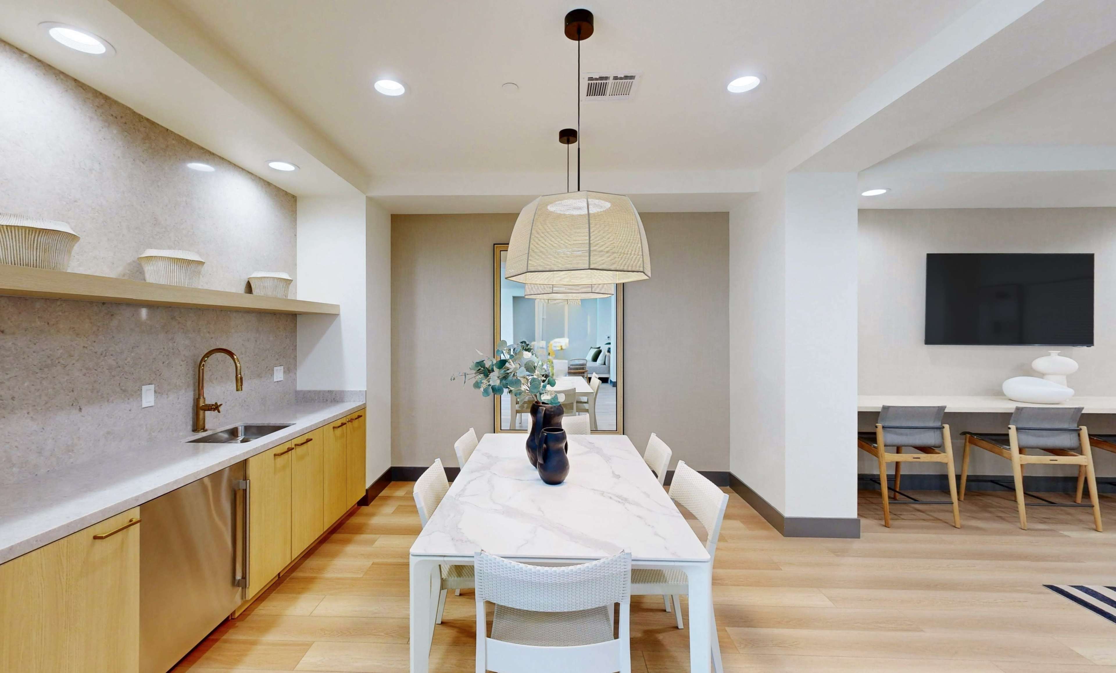 The image shows a modern kitchen and dining area with a long marble dining table, pendant lighting, and a minimalist design.