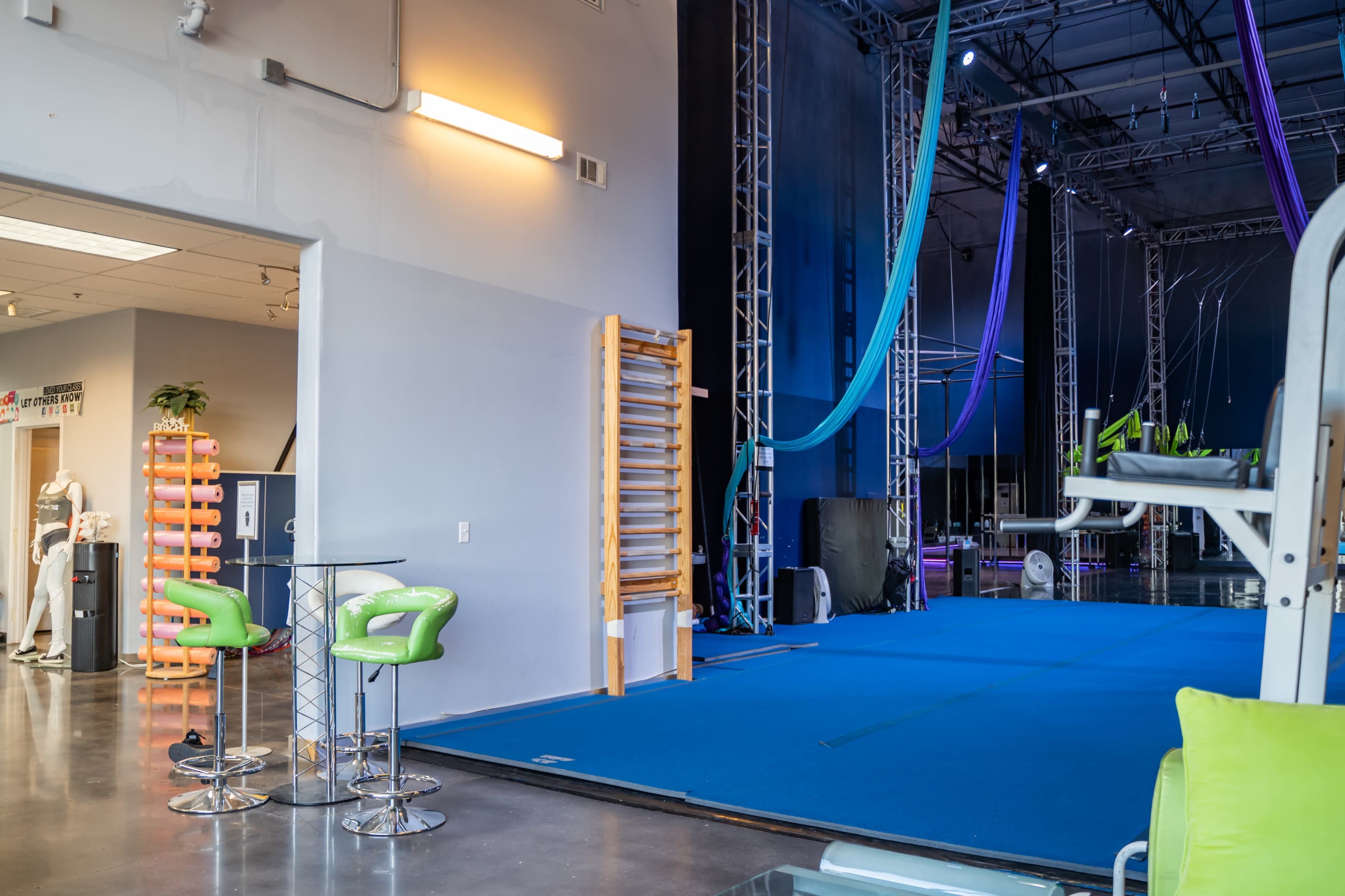A gym space with blue mats, exercise equipment, and aerial silks hanging from the ceiling.