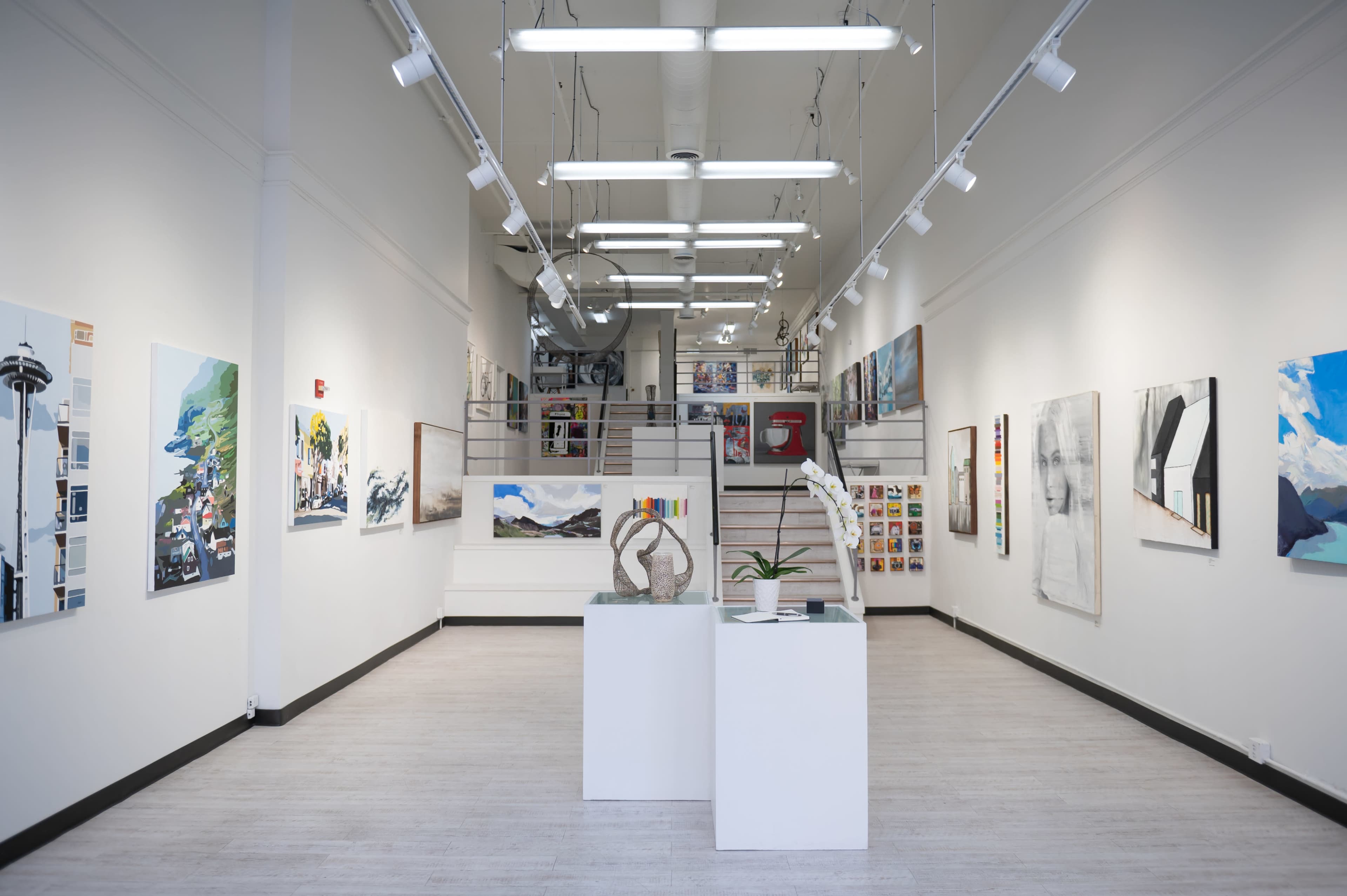 A contemporary art gallery with various paintings displayed on the walls and a sculpture positioned on a pedestal in the center.