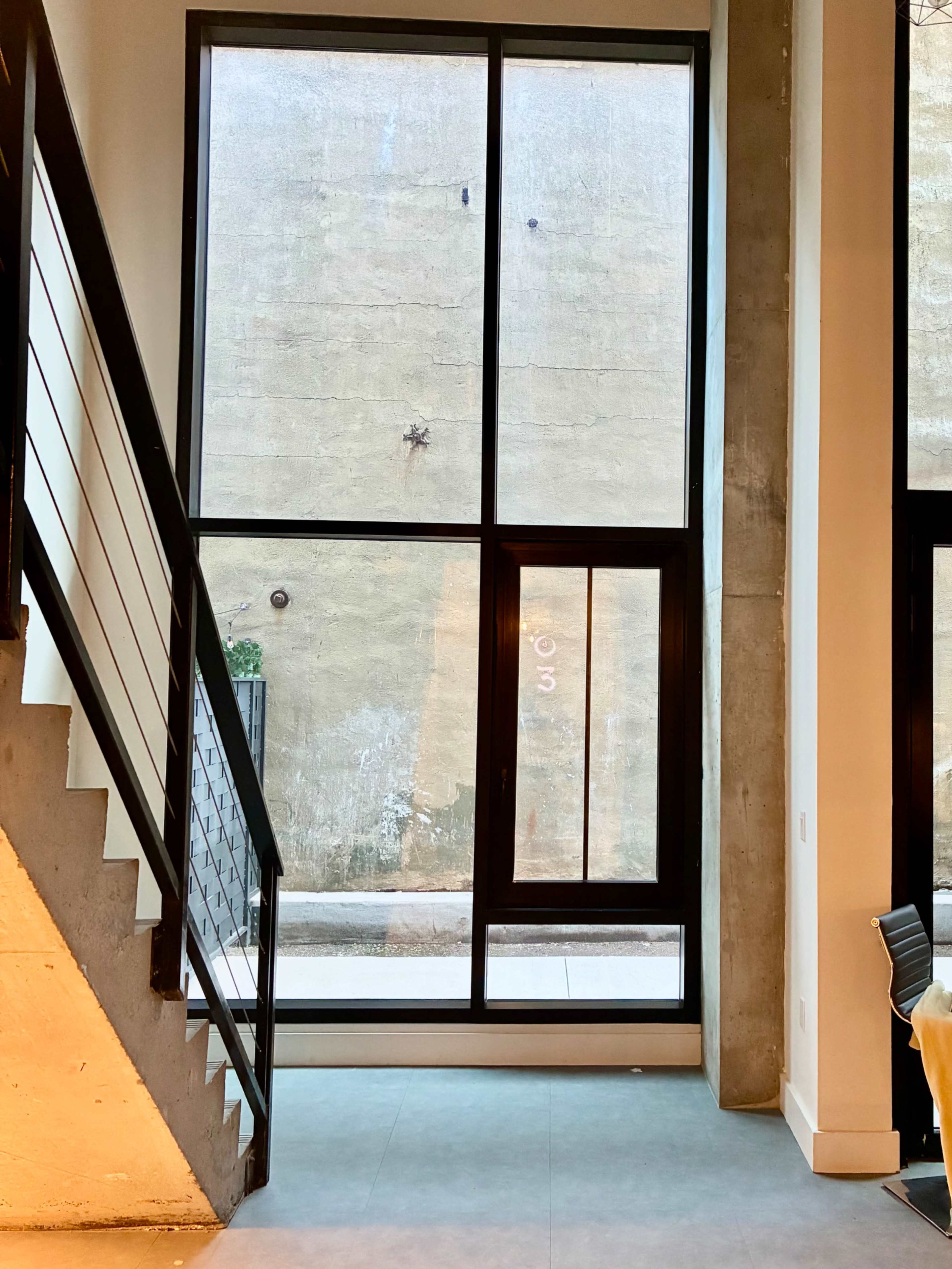 A staircase leads to a large window overlooking a textured, concrete wall.