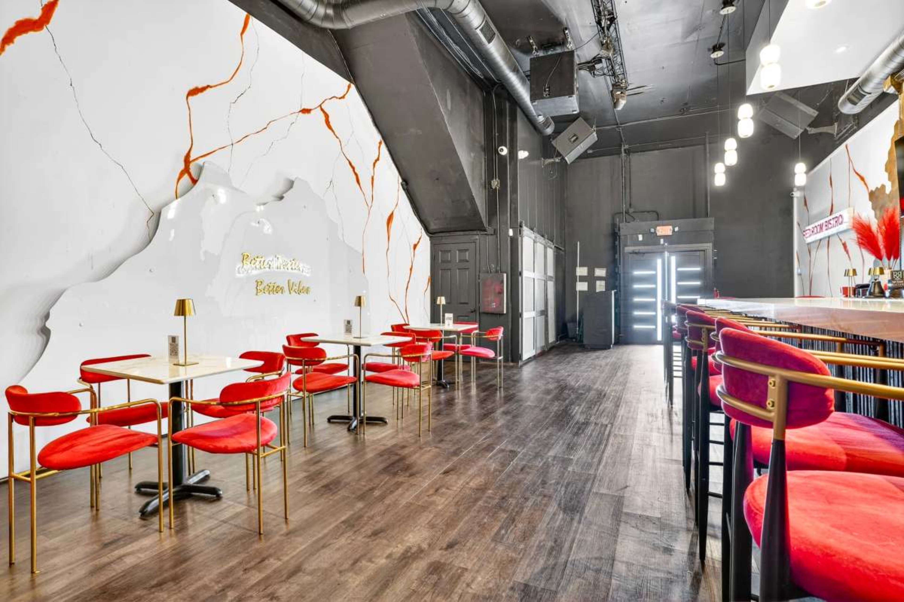 The image shows a modern café interior with red chairs and tables, a sleek bar area, and a wall featuring a marble-like design.