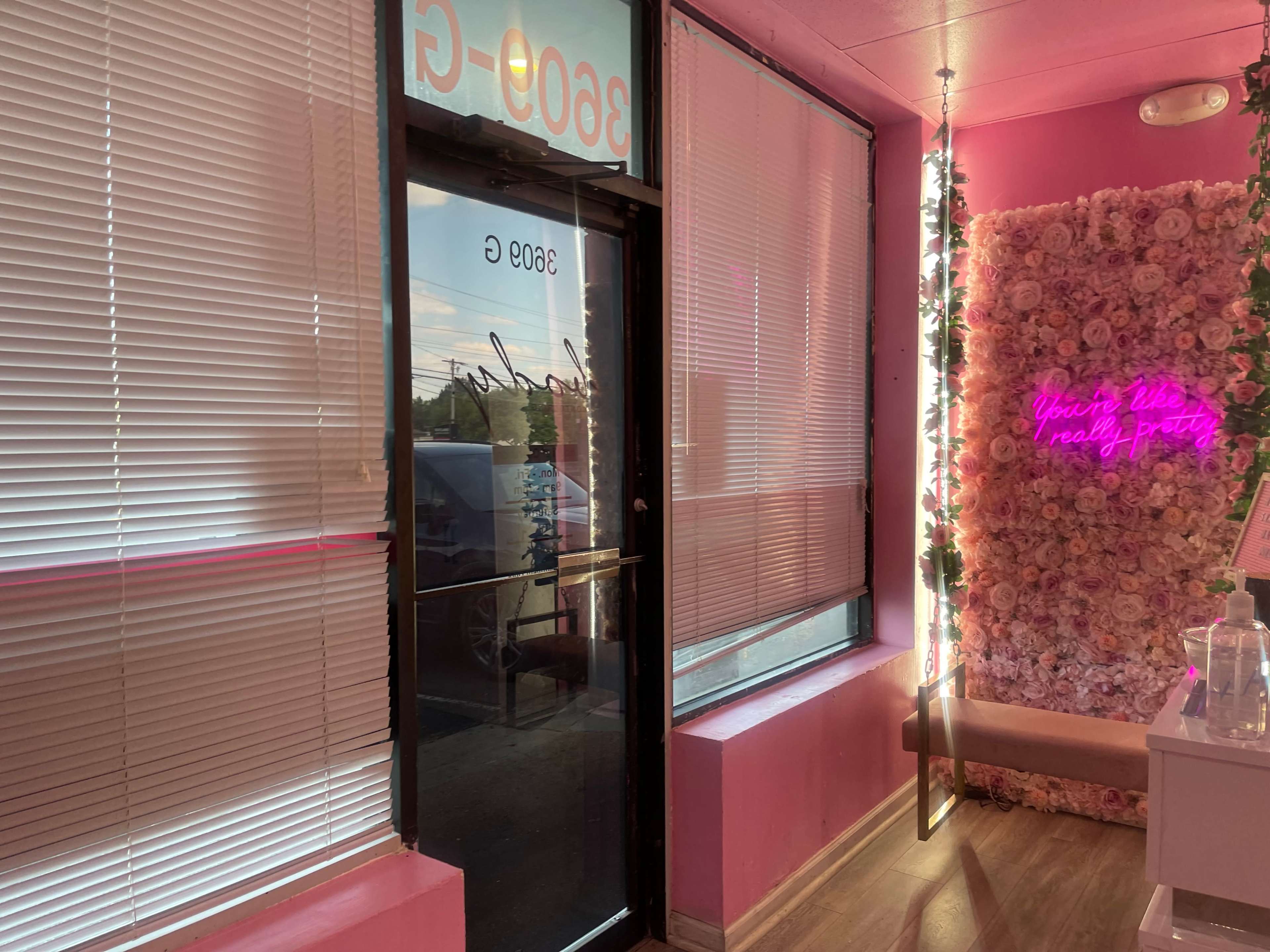 An entrance to a brightly colored room with pink walls, featuring a decorative flower wall and a neon sign.