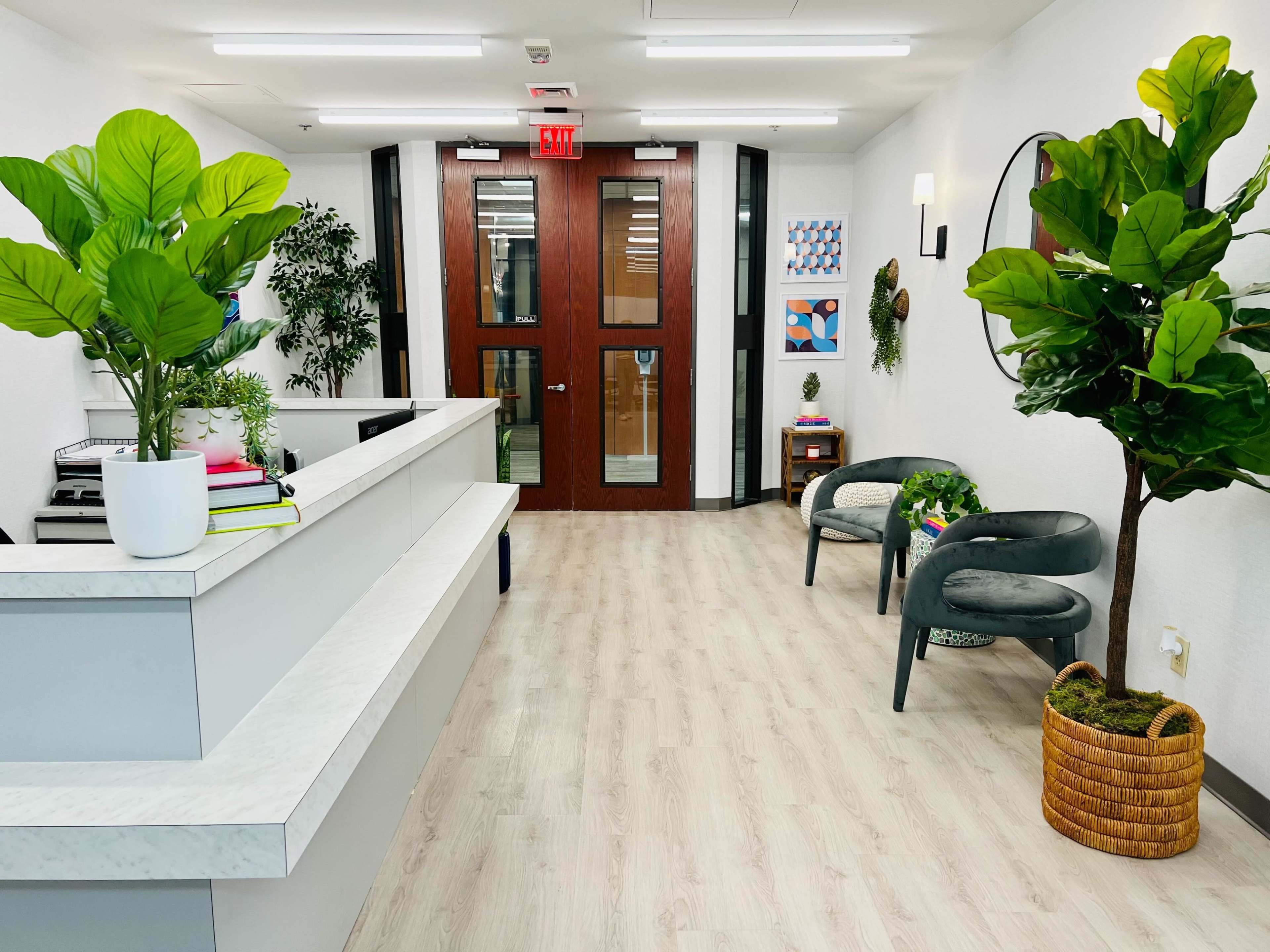 A modern reception area featuring a front desk, greenery, and a waiting area with chairs and decorative elements.